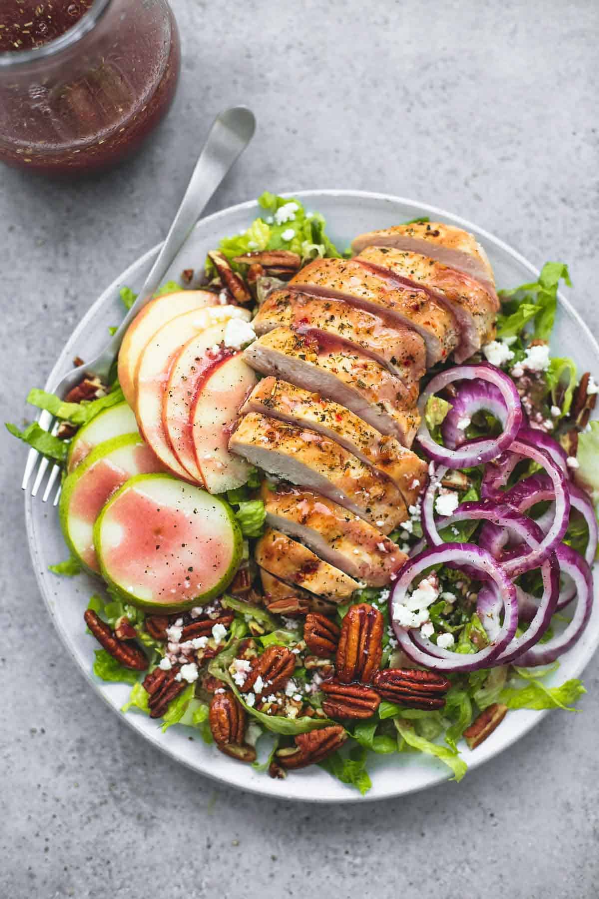 top view of Autumn harvest chicken salad with a fork on a plate with sweet and tangy apple cranberry dressing in a jar on the side.