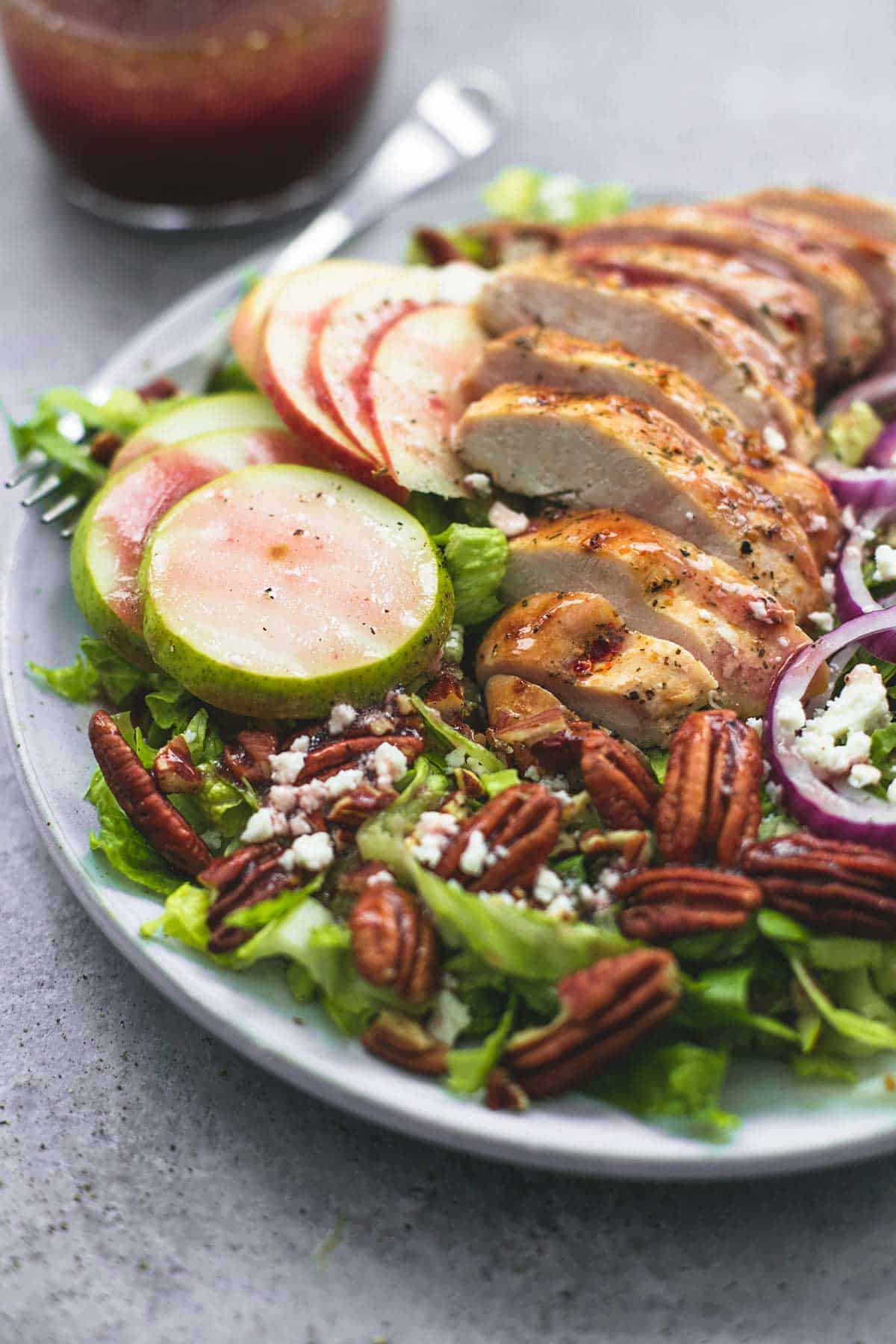 Autumn harvest chicken salad with a fork on a plate with sweet and tangy apple cranberry dressing on the side.