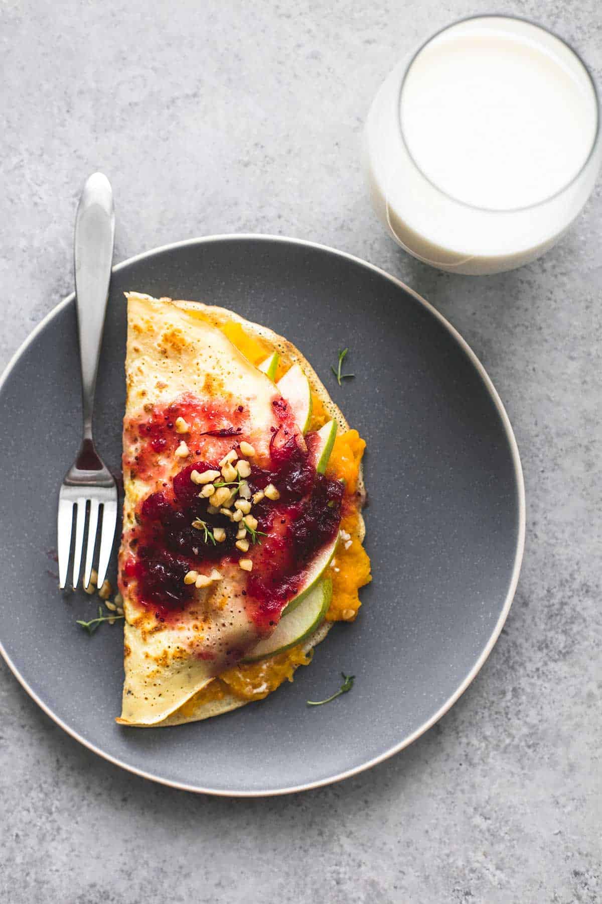 top view of a butternut squash & pear crepe with cranberry sauce with a fork on a plate with a glass of milk on the side.