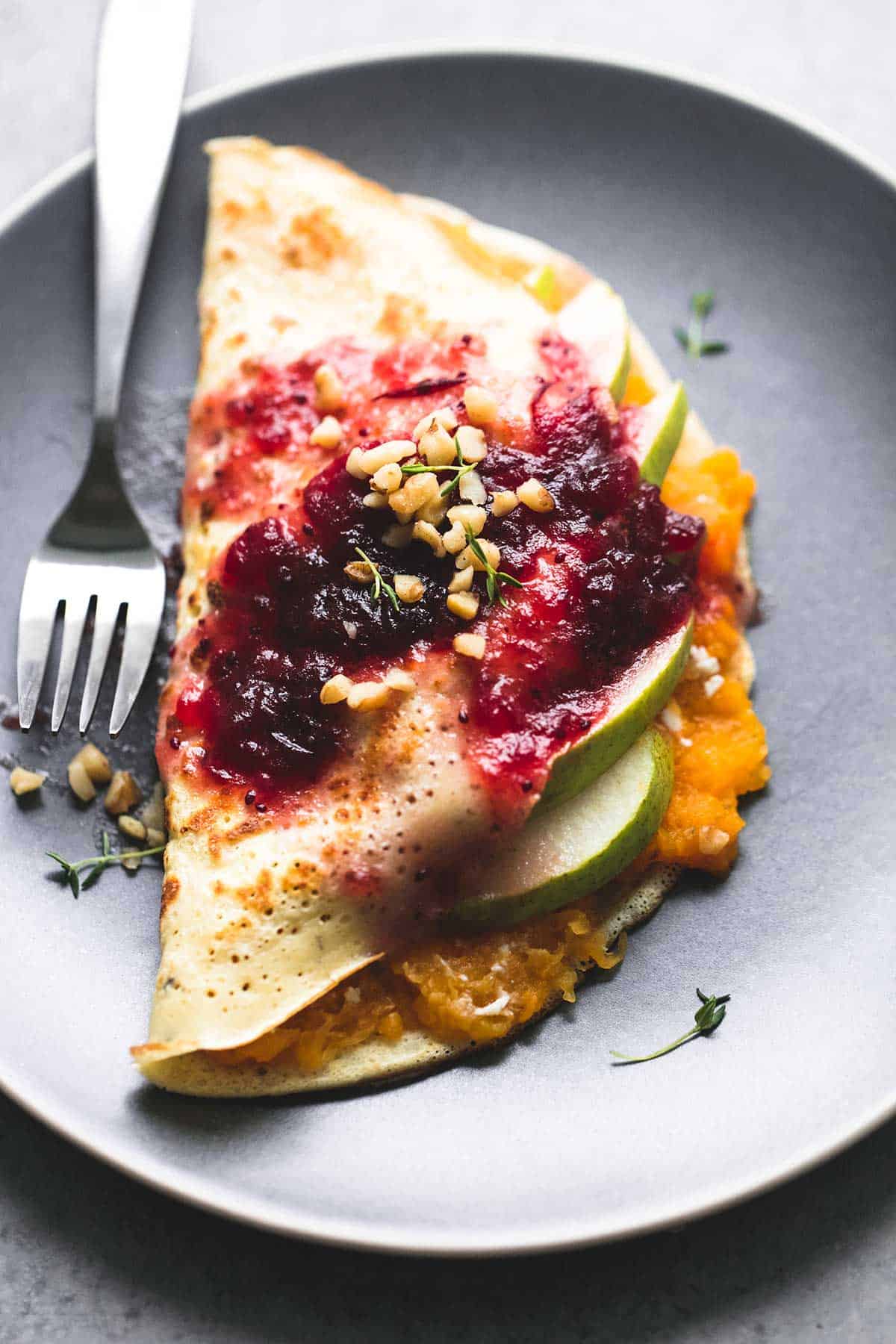 a butternut squash & pear crepe with cranberry sauce with a fork on a plate.