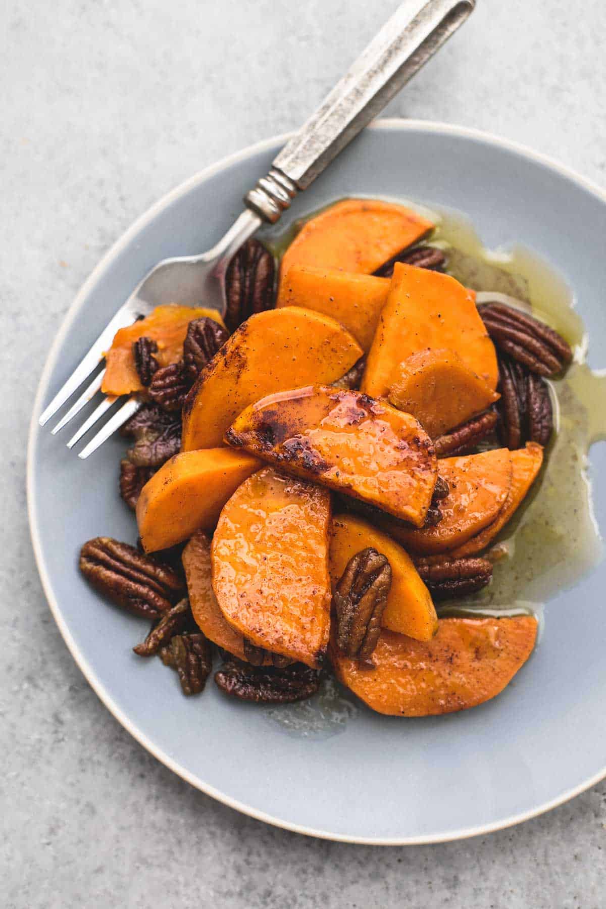 top view of baked Southern candied sweet potatoes with pecans and a fork on a plate.