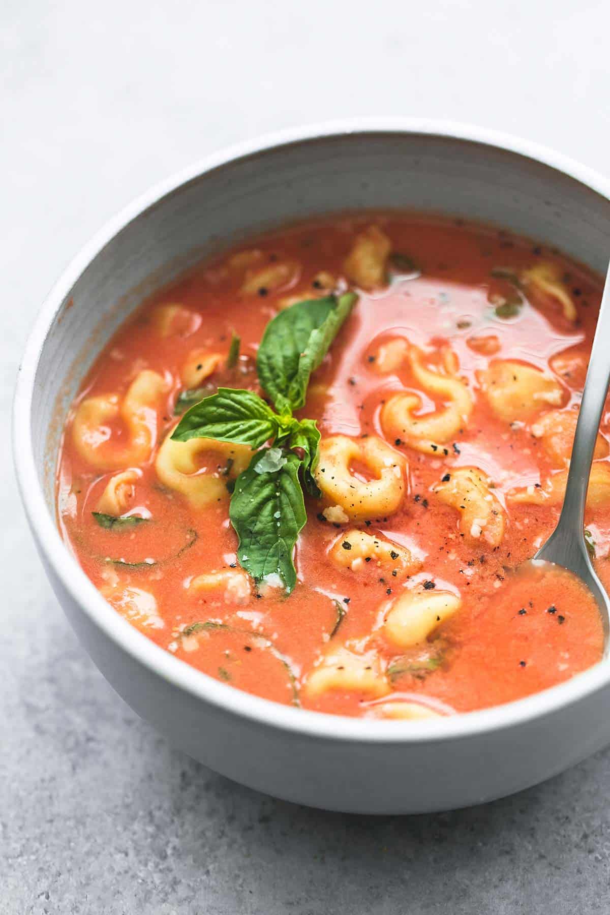 slow cooker tomato basil parmesan tortellini soup with a spoon in a bowl.