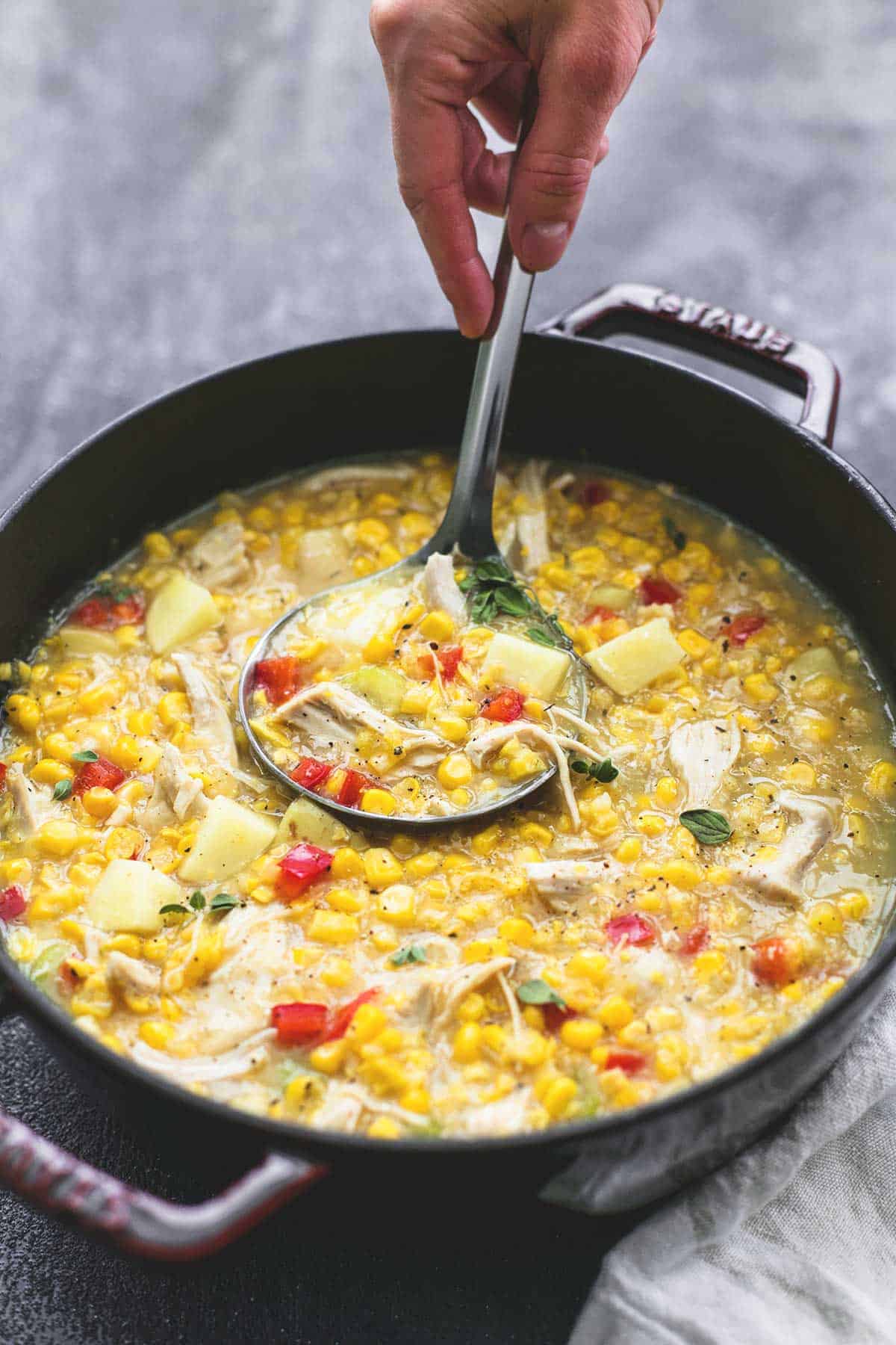 a hand scooping some leftover turkey corn chowder from a pan with a serving spoon.