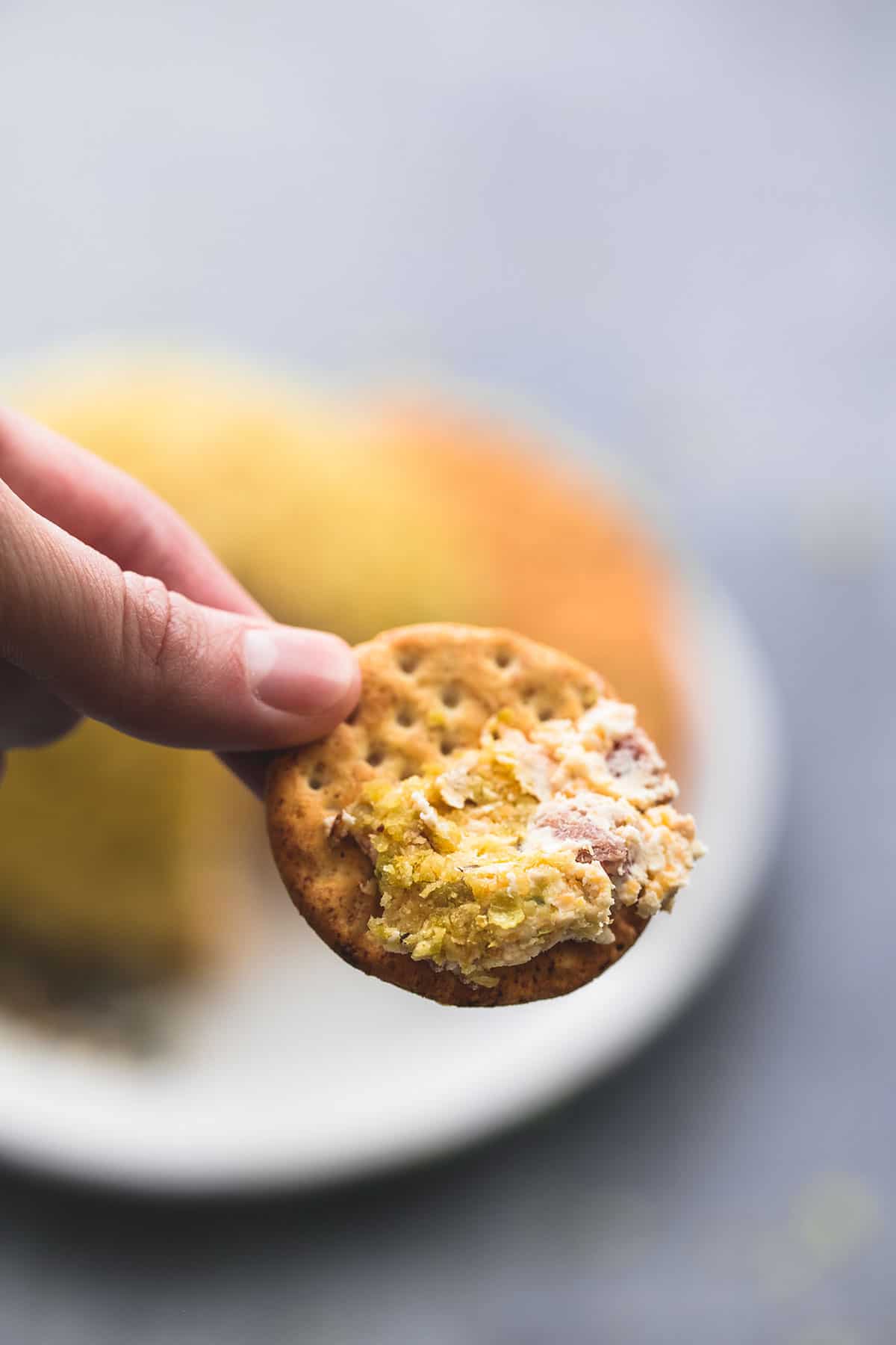 a hand holding a cracker dipped in cheddar bacon jalapeno cheeseball.