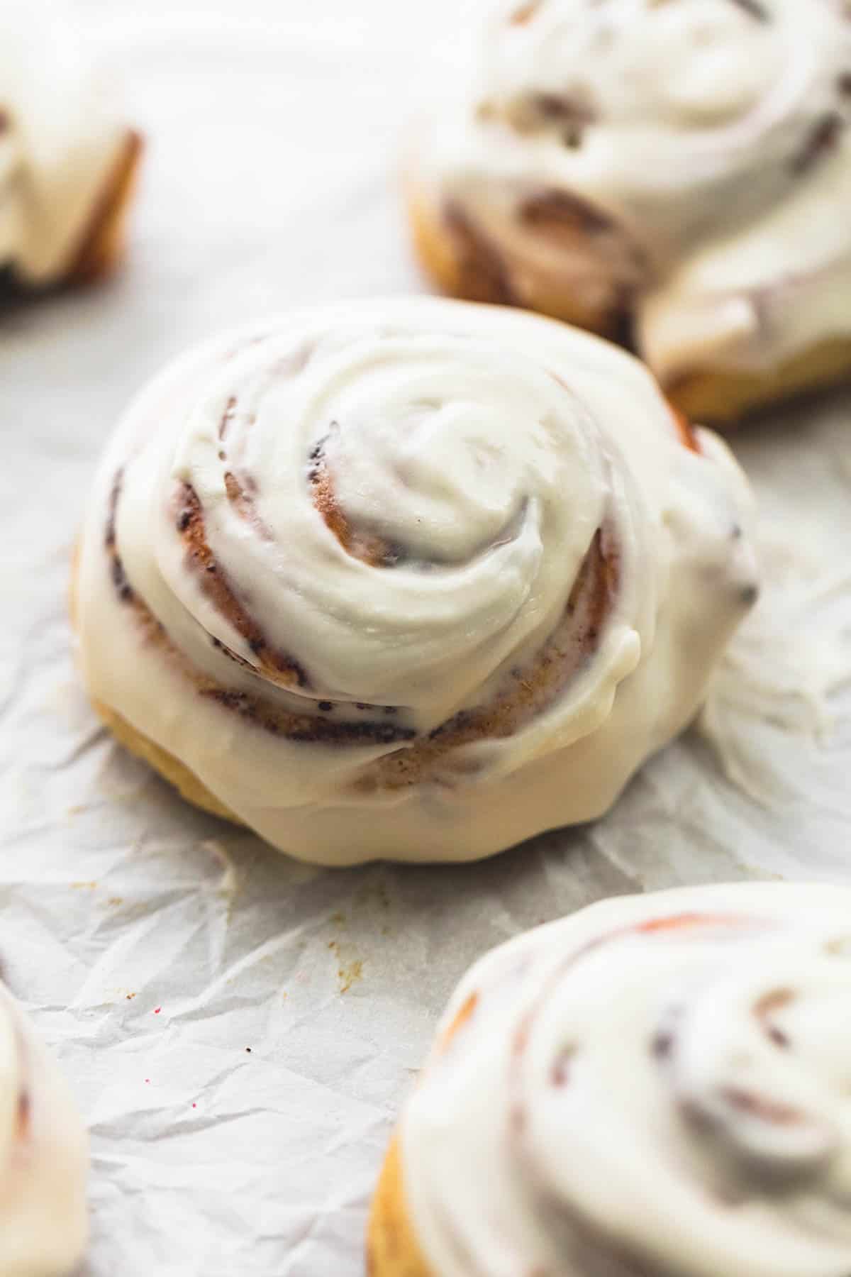 a cinnamon roll topped with icing with more iced rolls around it.