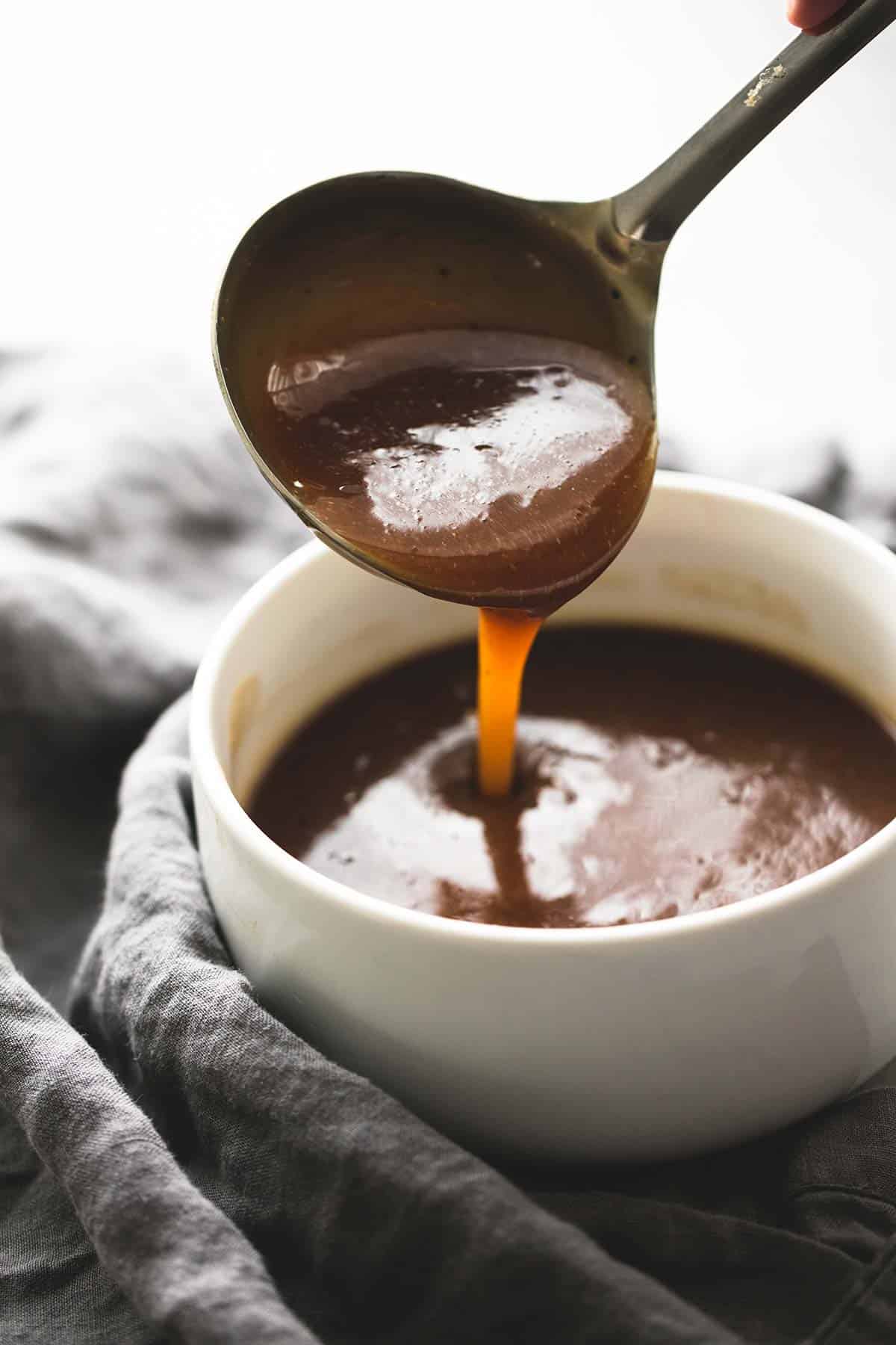 a serving spoon of gravy being poured into a bowl.