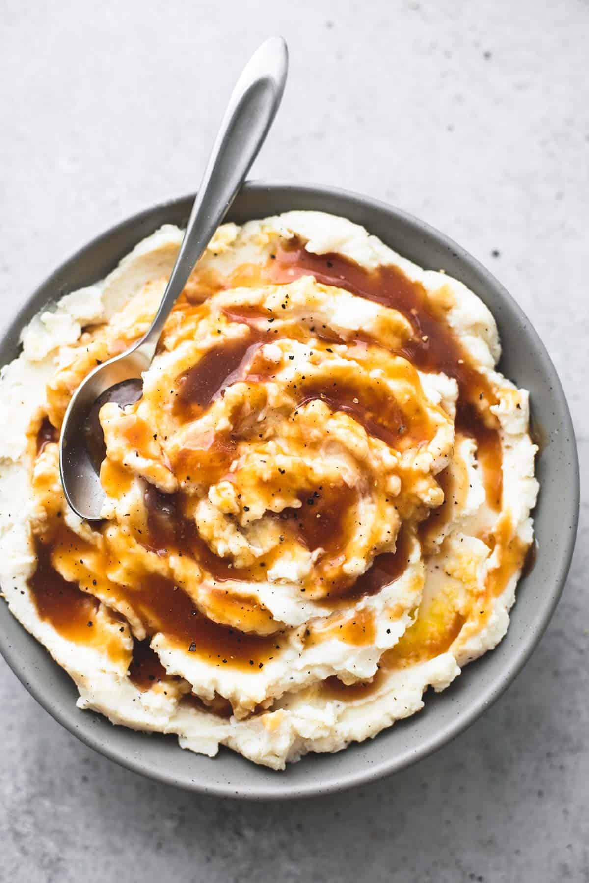 top view of beef broth brown gravy on top of mashed potatoes with a spoon in a bowl.