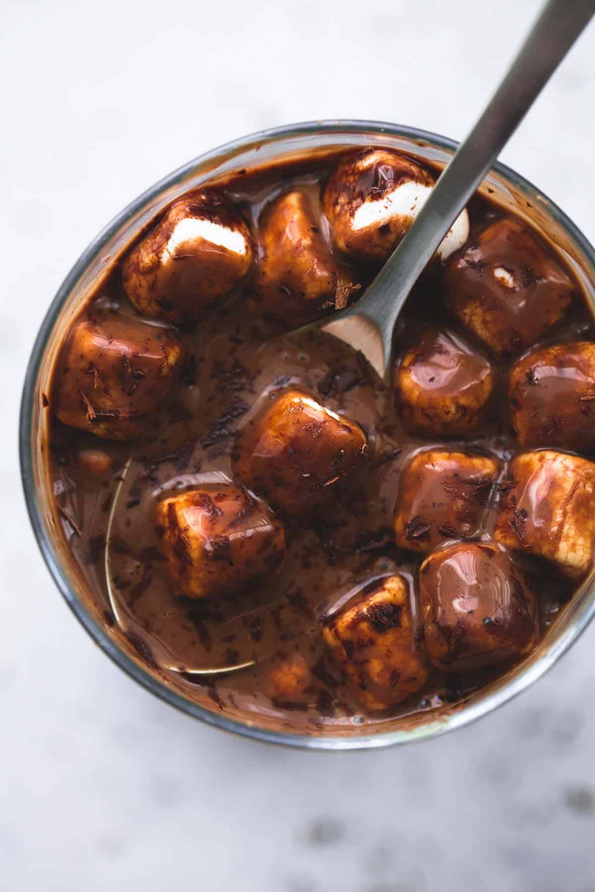 close up top view of extra thick hot chocolate with a spoon and marshmallows in a glass.