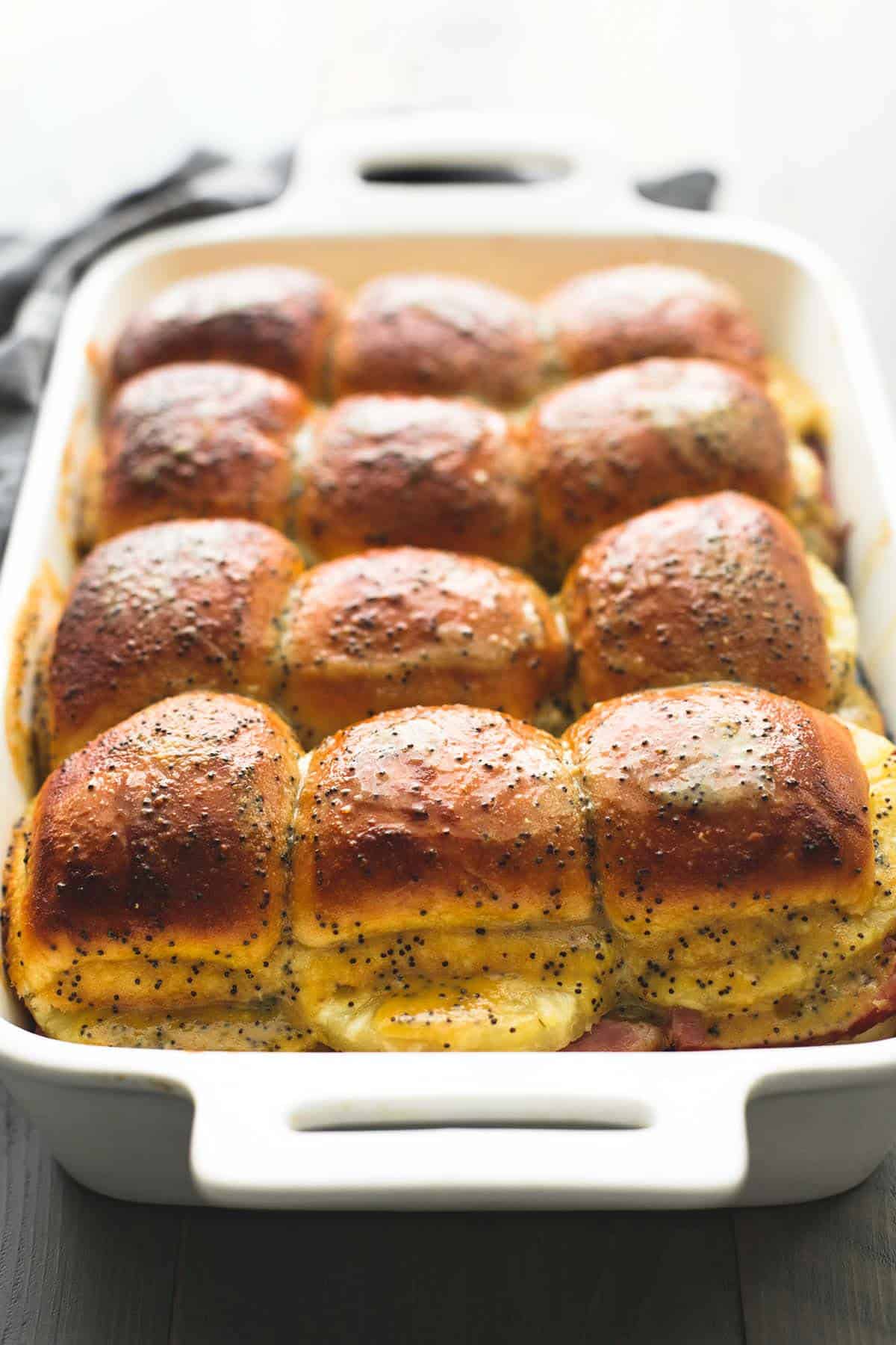 ham & swiss cheese sliders in a baking pan topped with poppyseeds and butter.