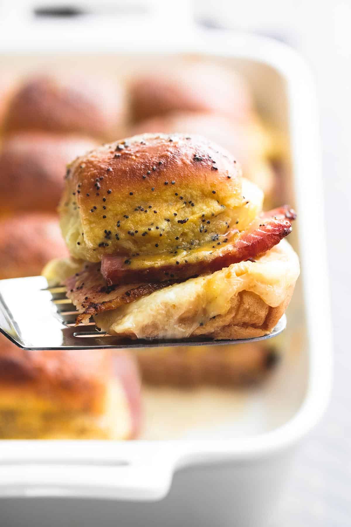 a spatula holding a slider with more sliders in a baking pan faded in the background.