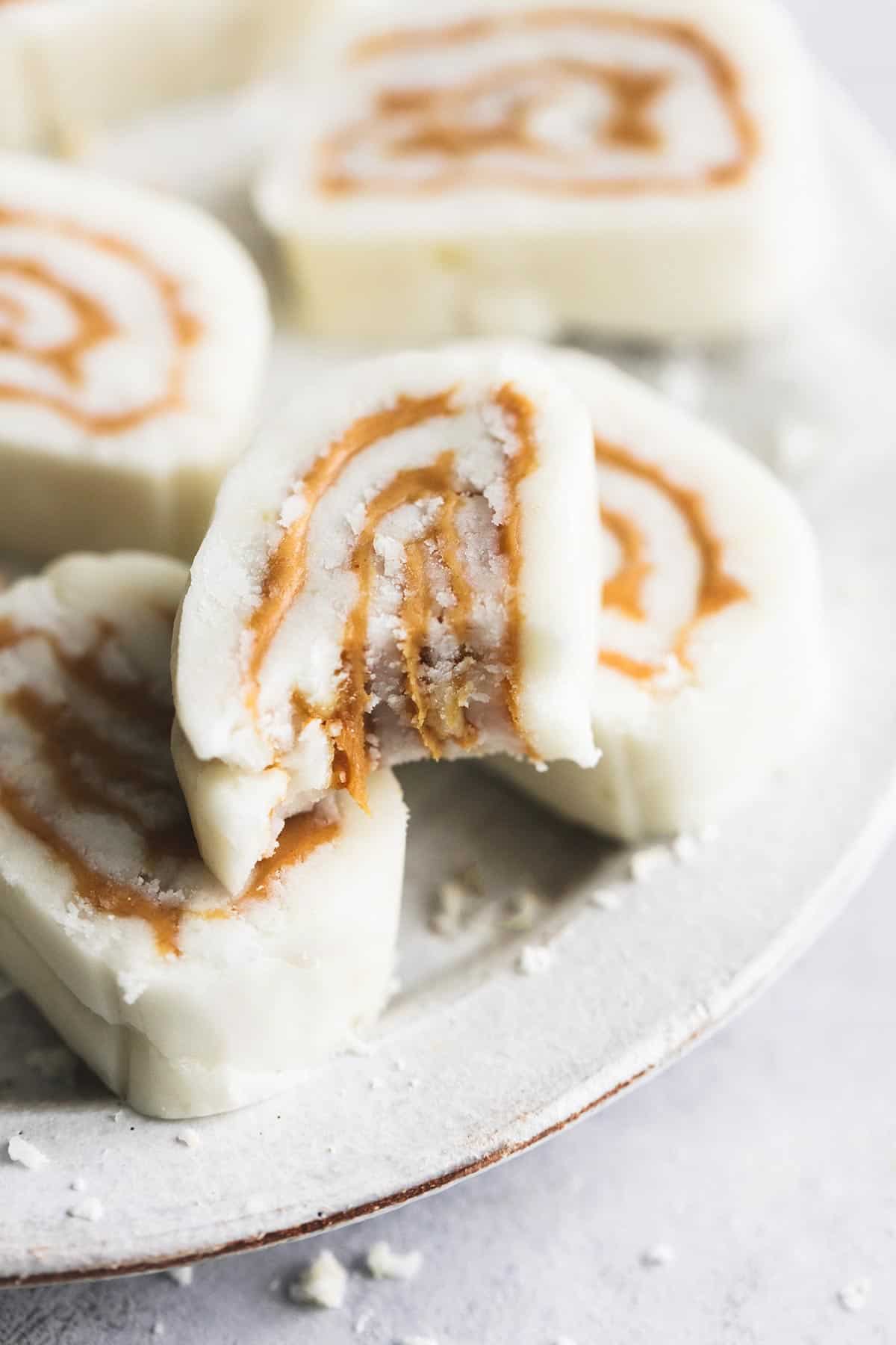 a piece of old fashioned potato candy with a bite missing sitting on top of more candy on a plate.