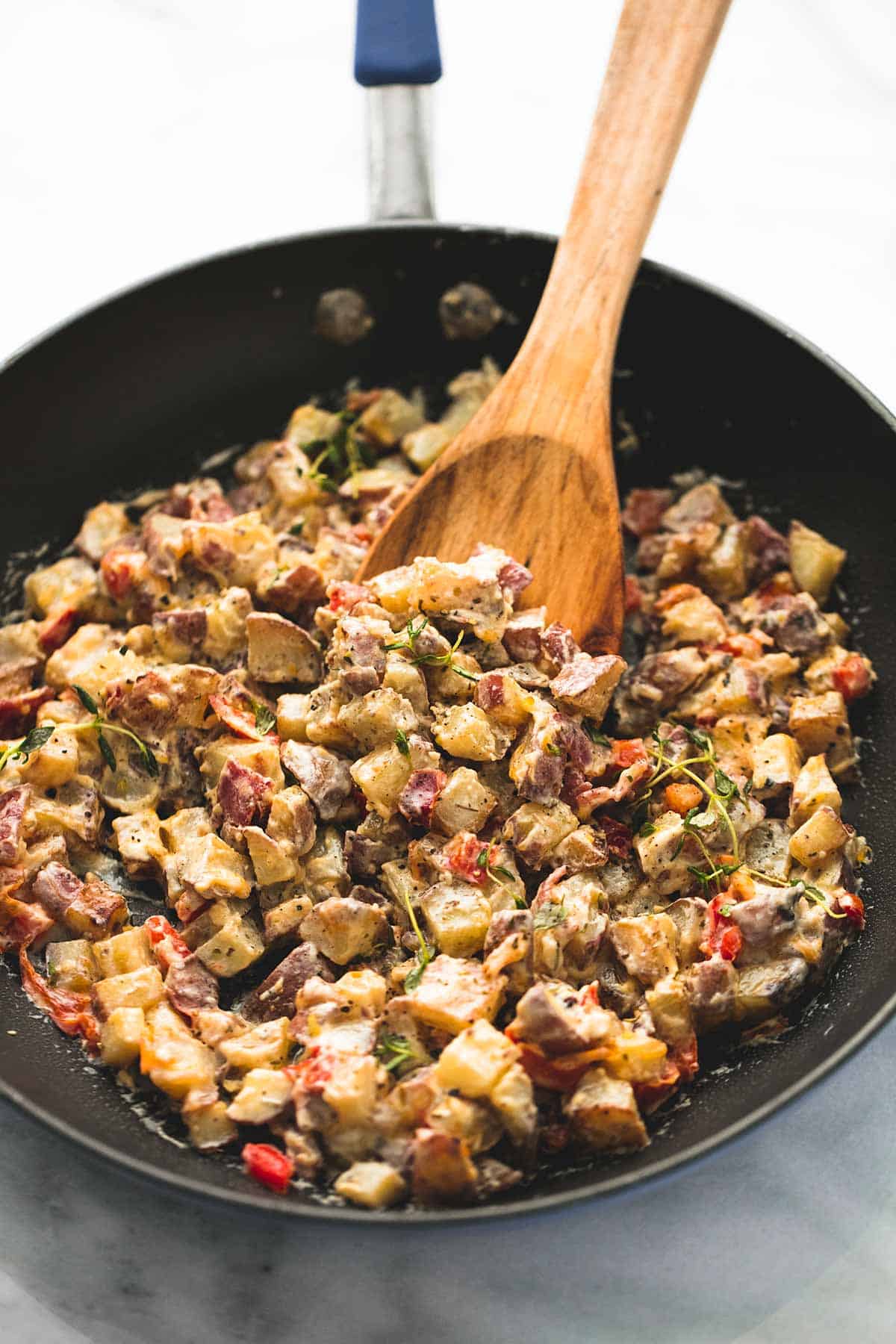 garlic herb potato hash with a wooden serving spoon in a skillet.