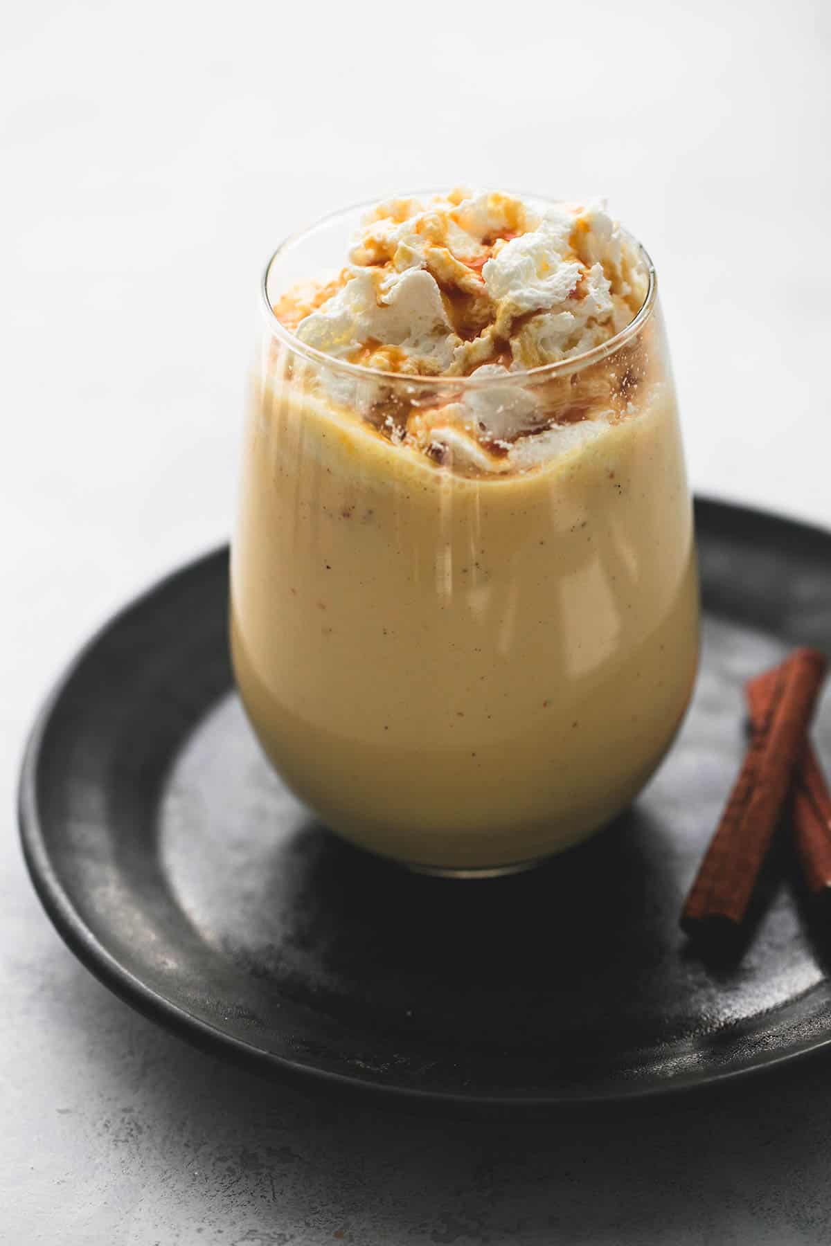pumpkin nog in a glass with cinnamon sticks on the side all on a plate.