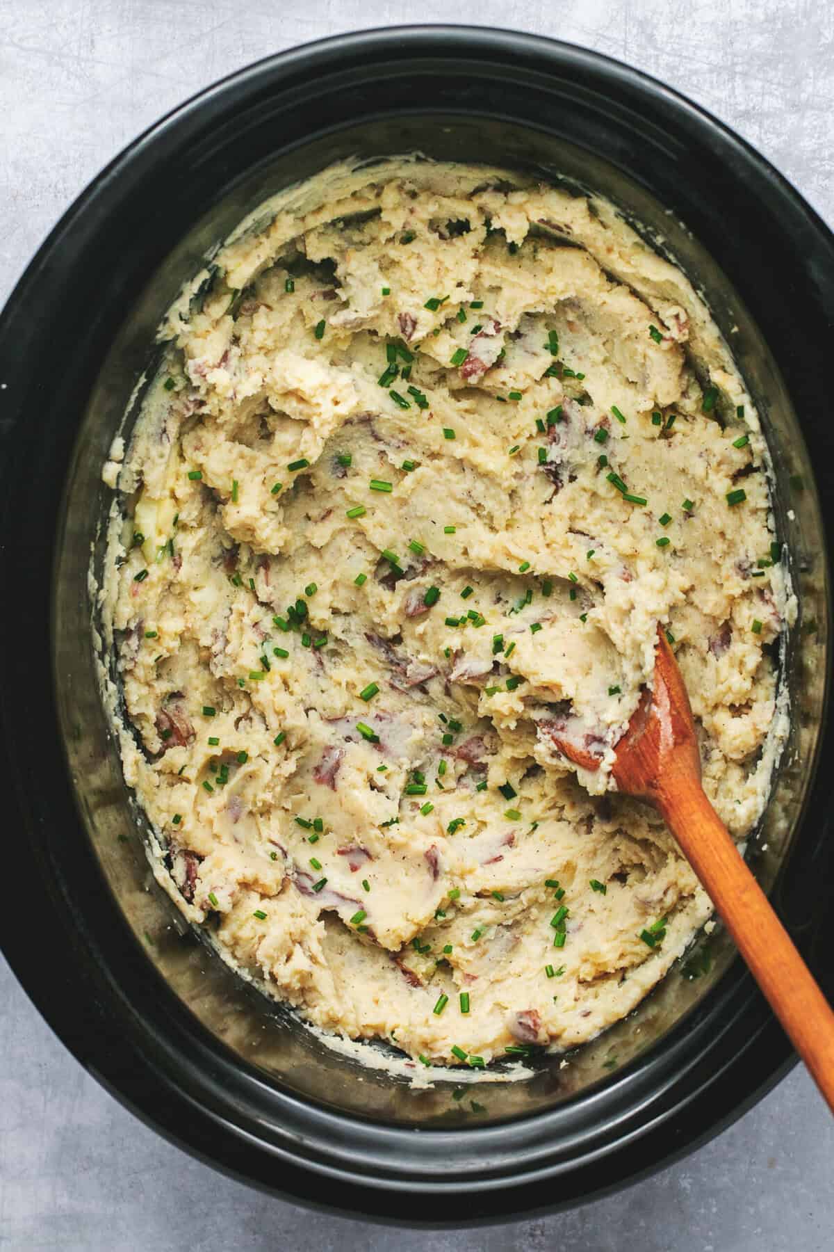 Overhead of slow cooker mashed potatoes in a slow cooker with a wooden spoon.