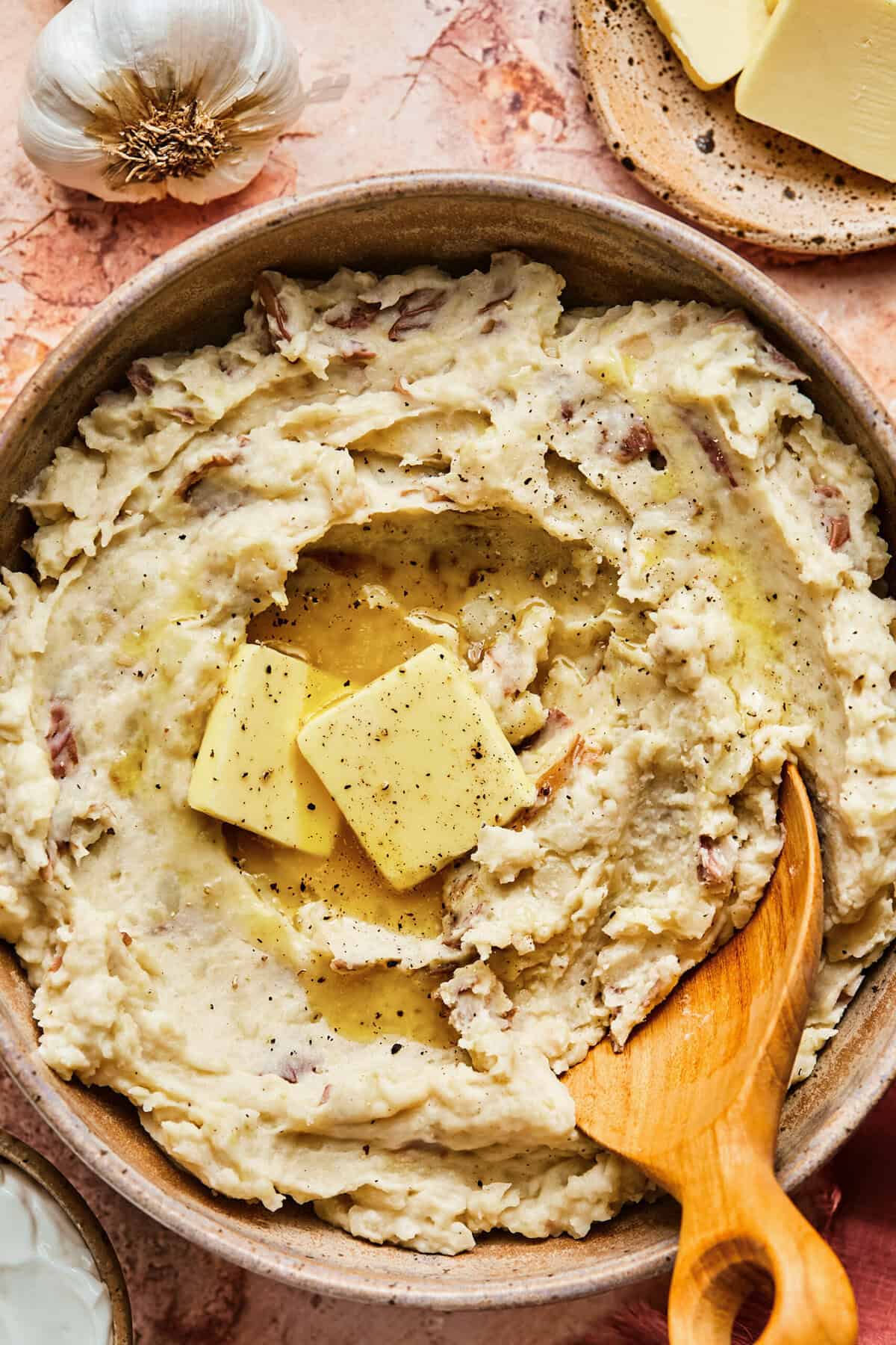 Overhead of garlic sour cream mashed potatoes and a wooden serving spoon in a ceramic serving bowl.
