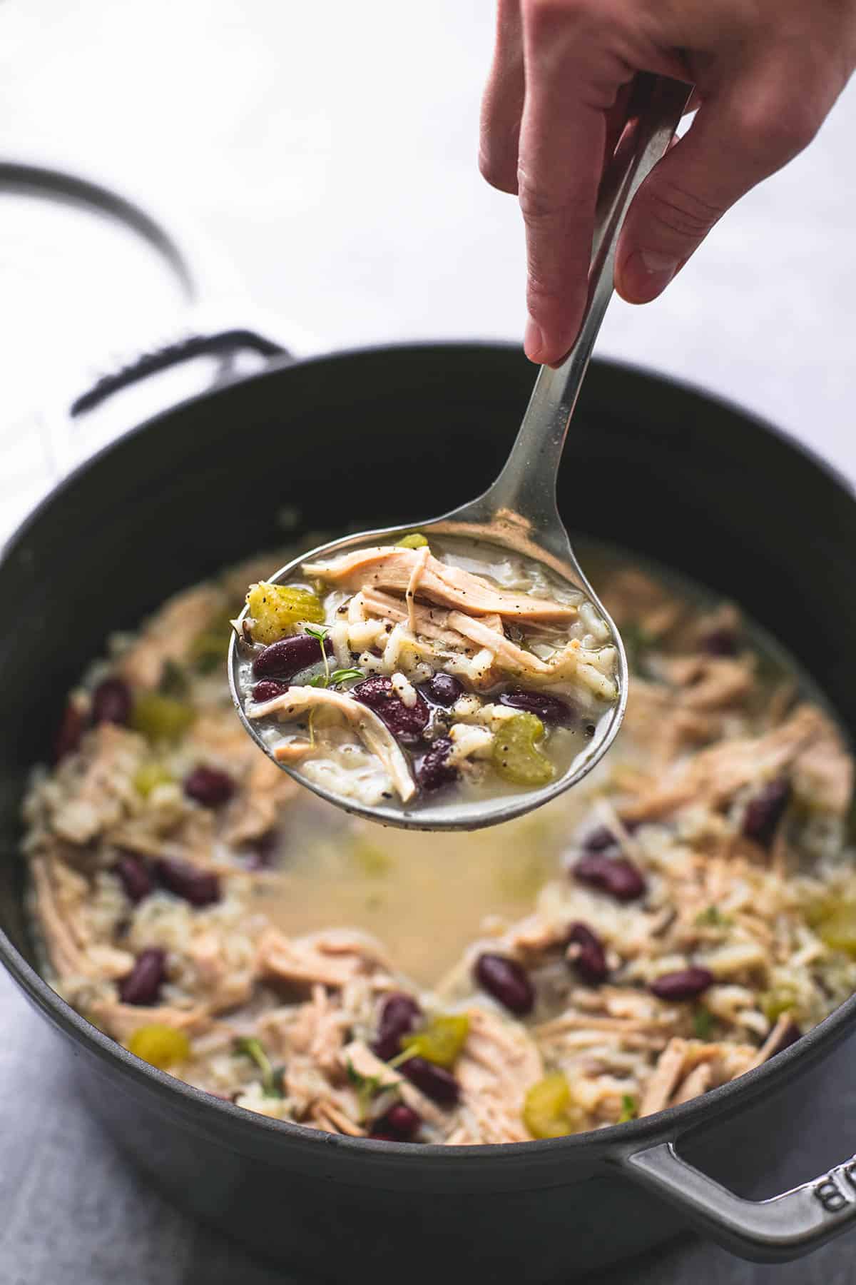 a hand holding a serving spoon of healthy turkey wild rice soup above a pan of more soup.