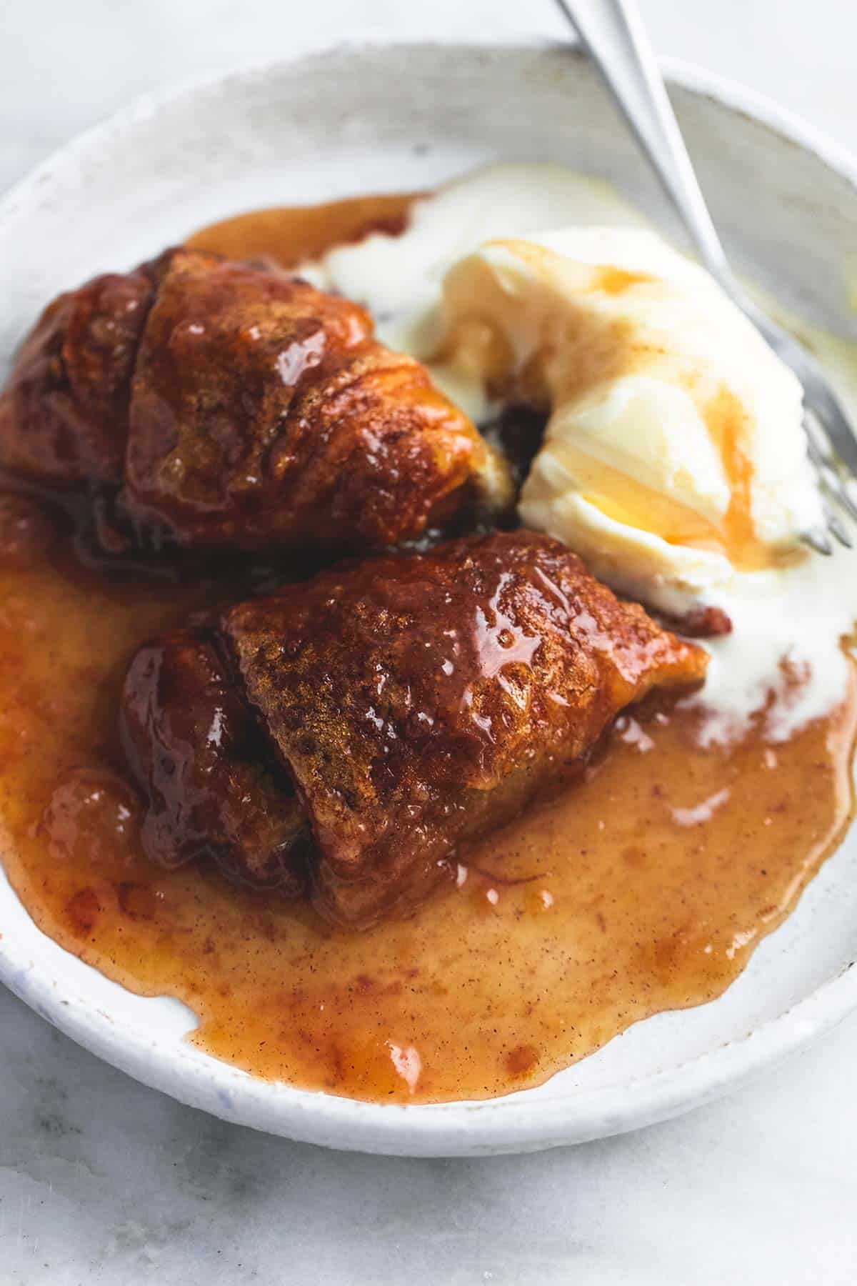 close up of cobbler with vanilla ice cream with caramel syrup on top and a fork on a plate.