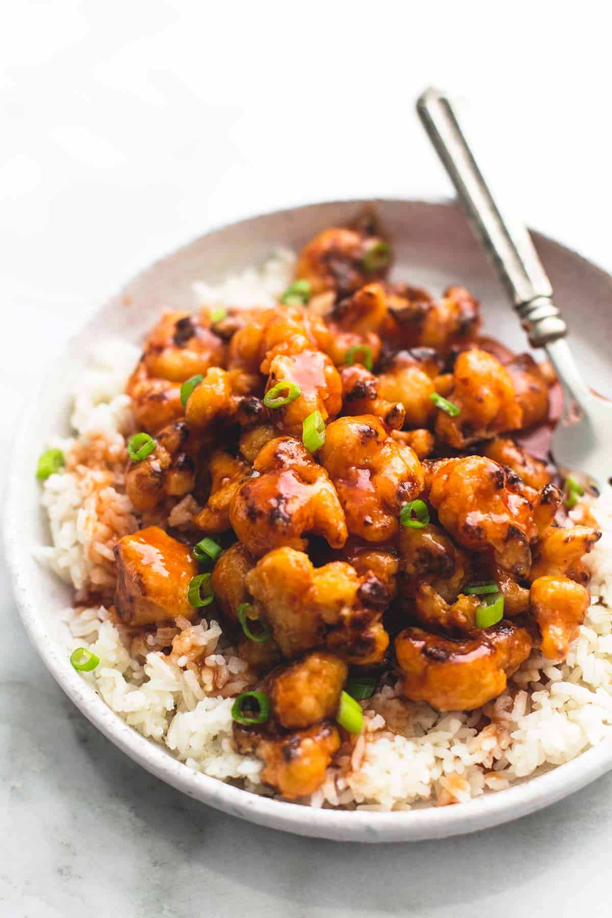 baked sweet & sour cauliflower on rice with a fork on a plate.