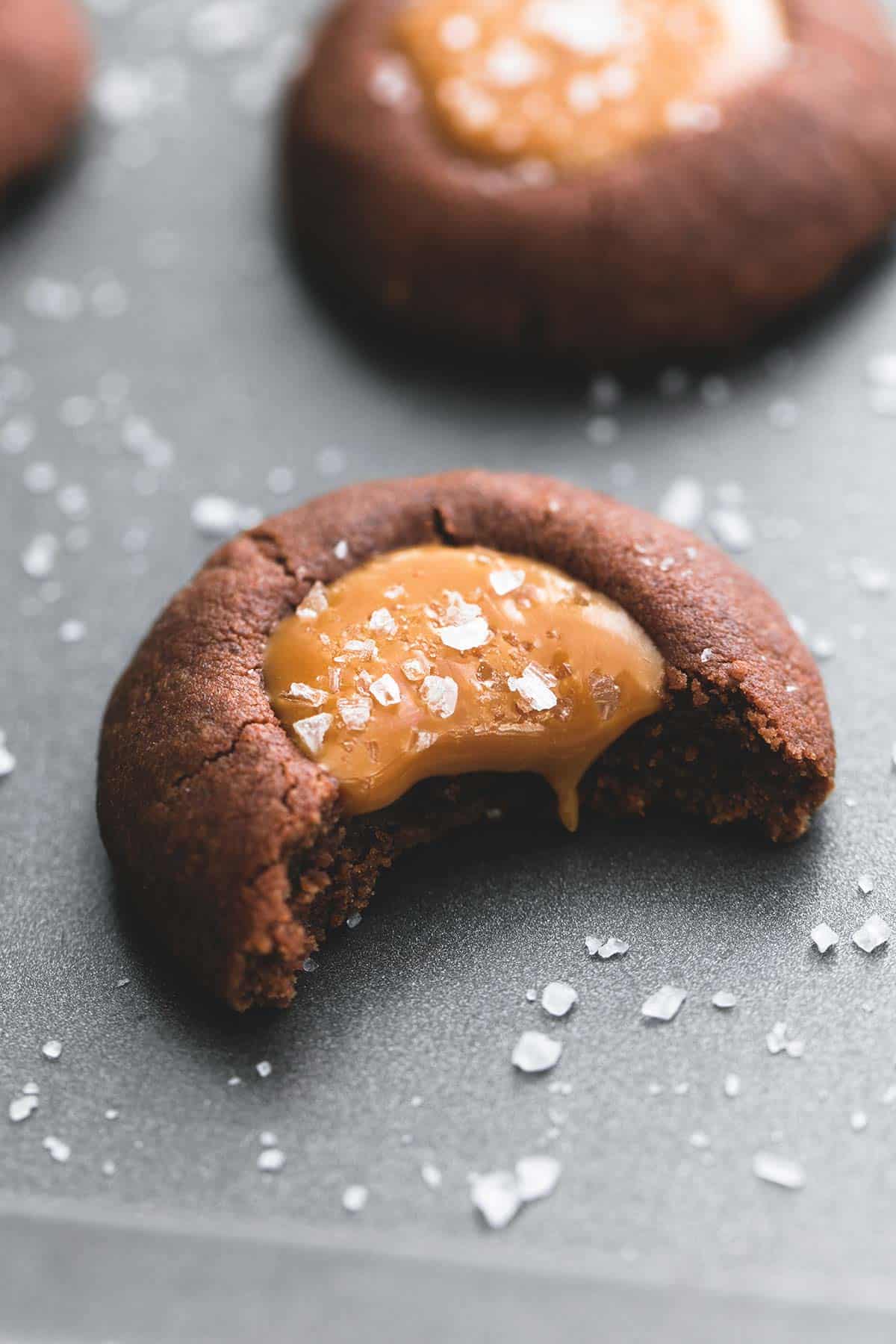 a salted caramel chocolate thumbprint cookie with a bite missing with more cookies in the background.