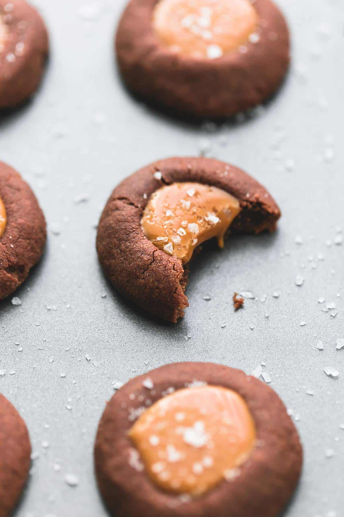 a salted caramel chocolate thumbprint cookie with a bite missing with more cookies around it.