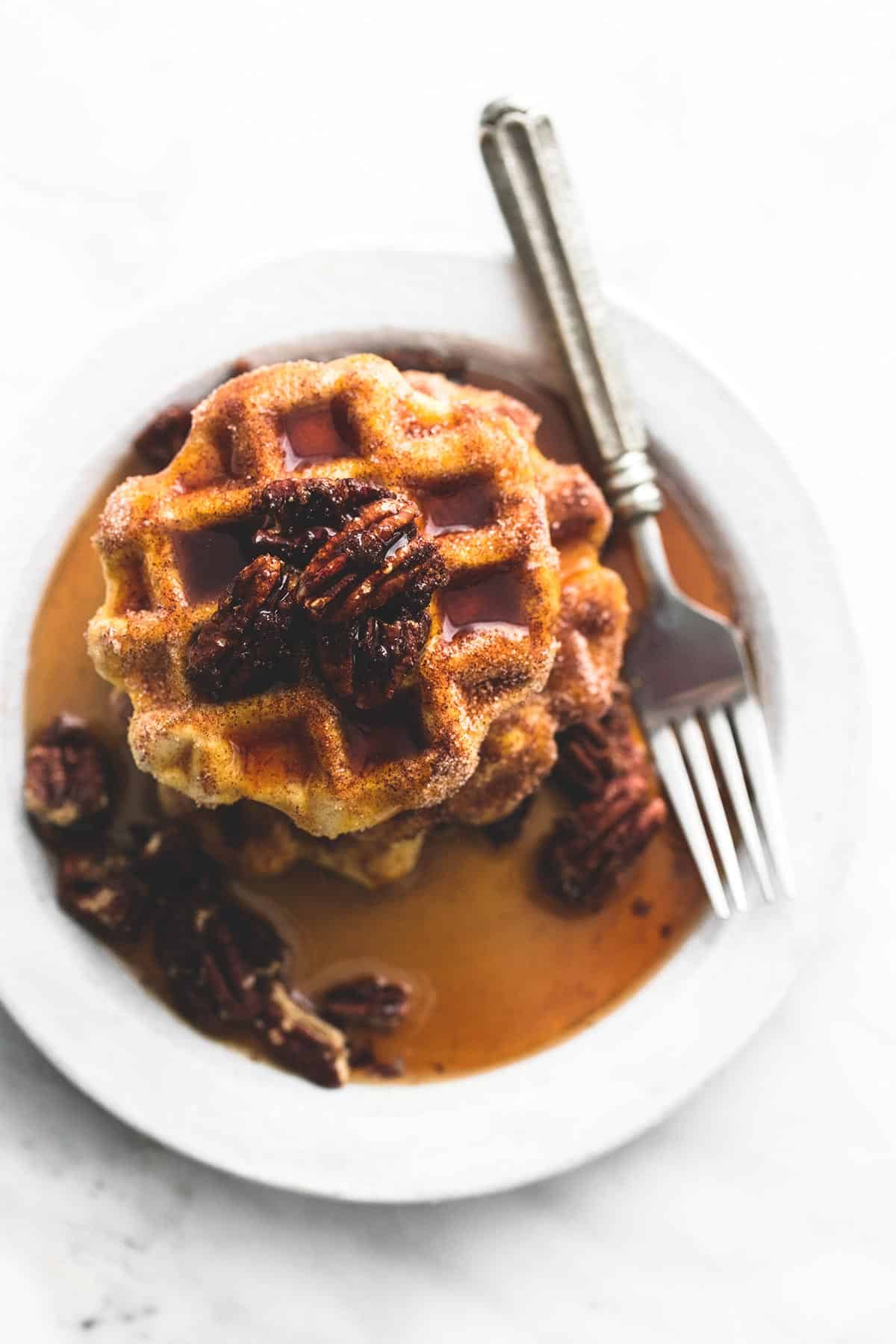 top view of cinnamon sugar biscuit waffles topped with candied pecans and syrup with a fork on a plate.