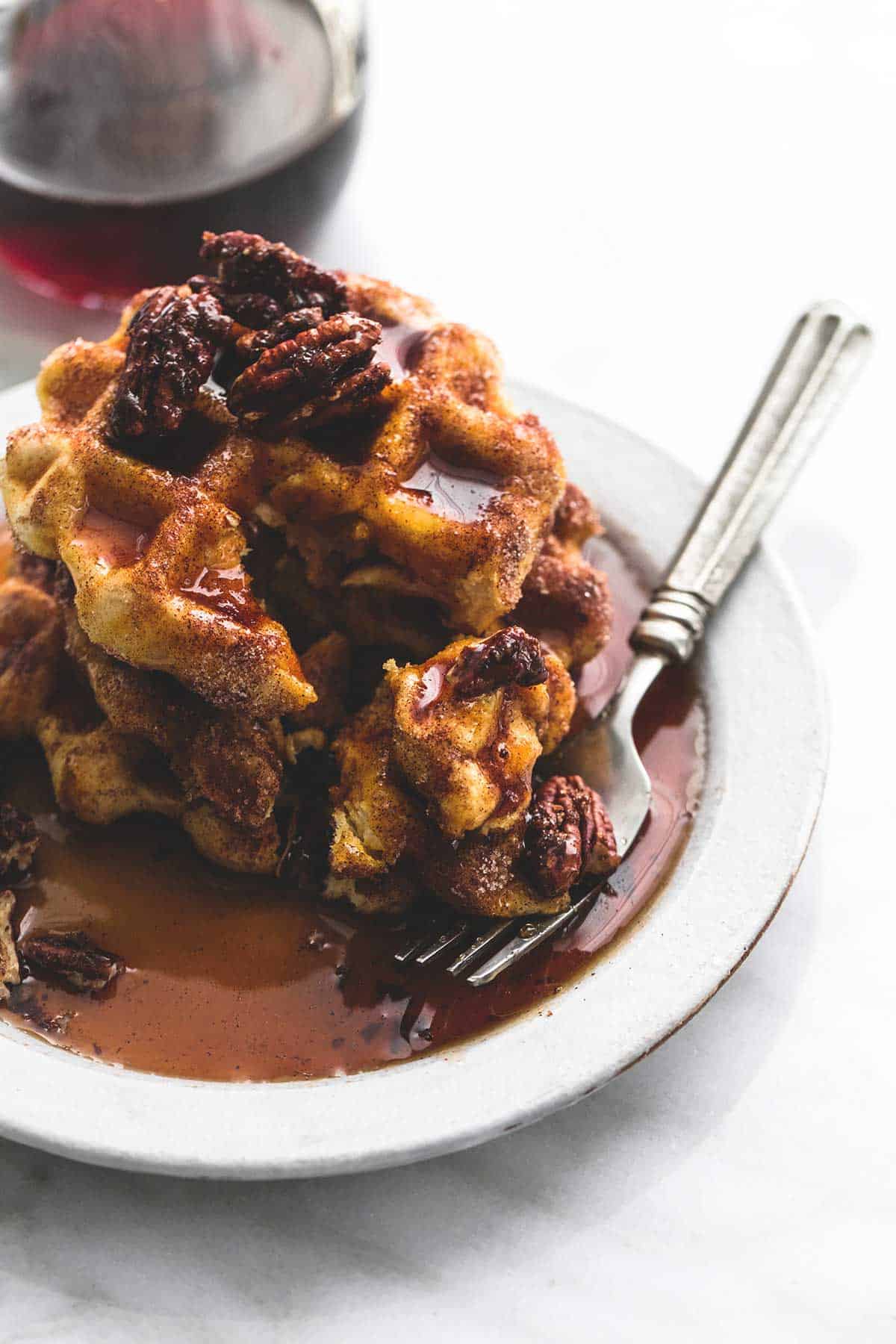 cinnamon sugar biscuit waffles topped with candied pecans and syrup with a fork on a plate.