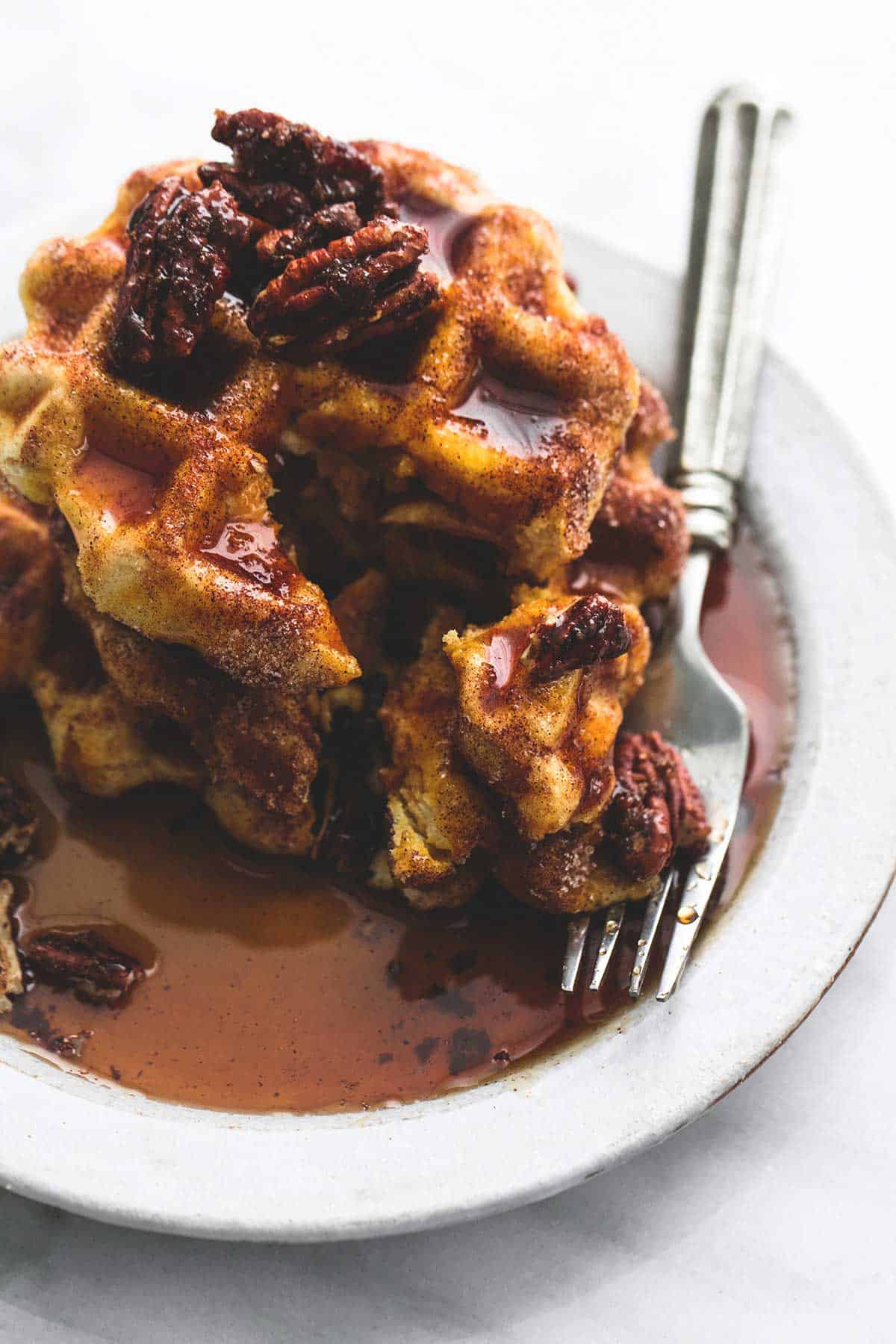 cinnamon sugar biscuit waffles with candied pecan topping with a fork on a plate.