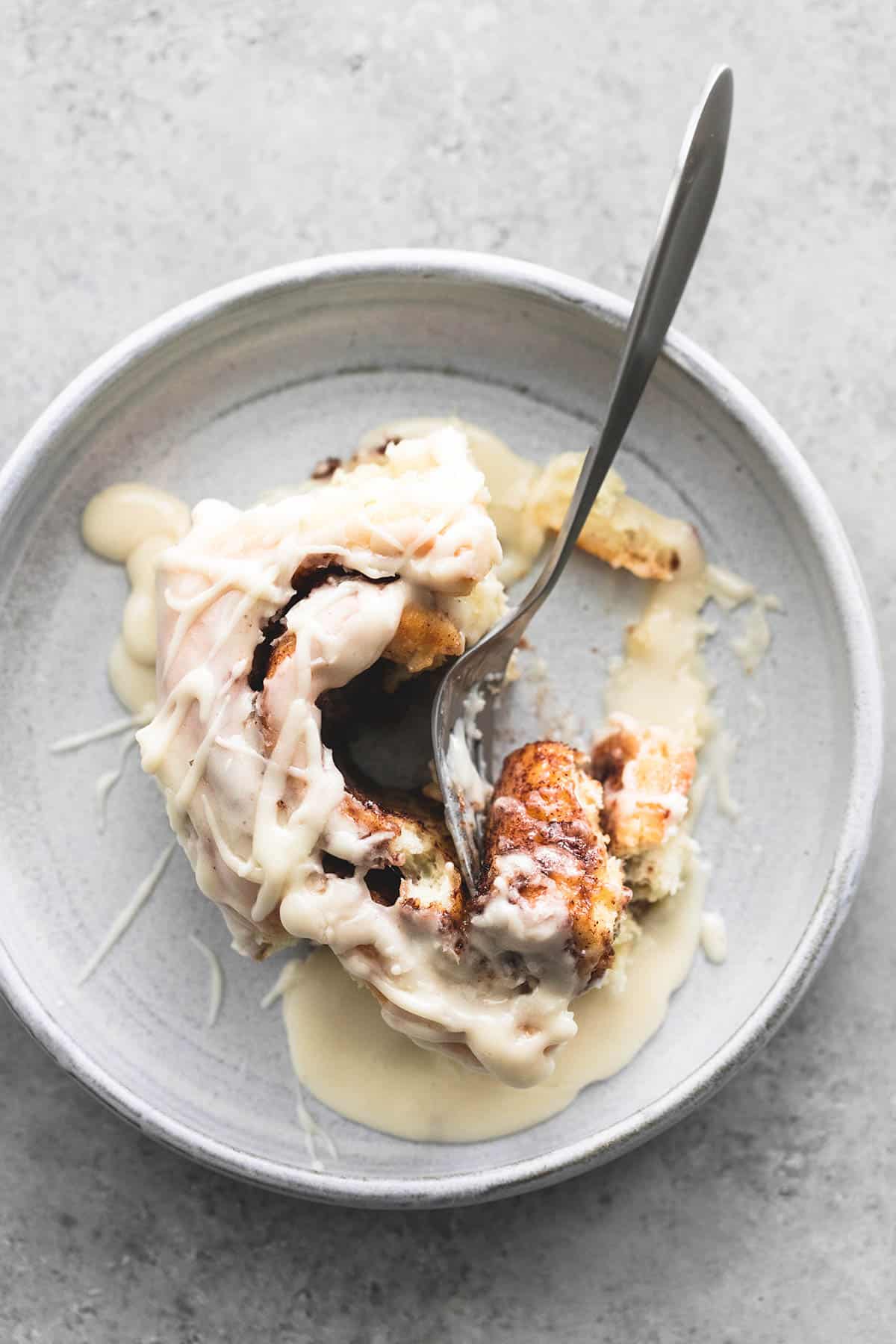 top view of a cream cheese cinnamon roll with a fork in between a bite and the rest of the roll on a plate.