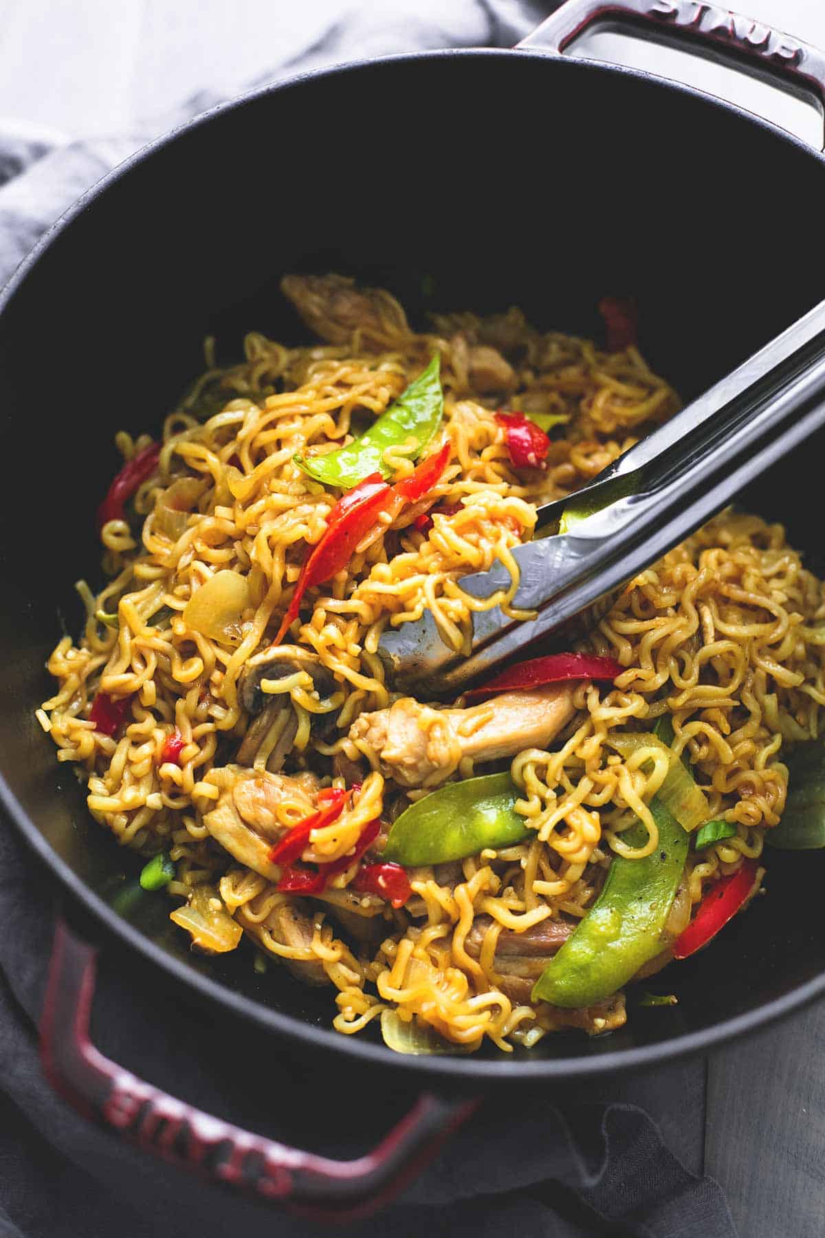 top view of chicken & veggie ramen with tongs in a wok.