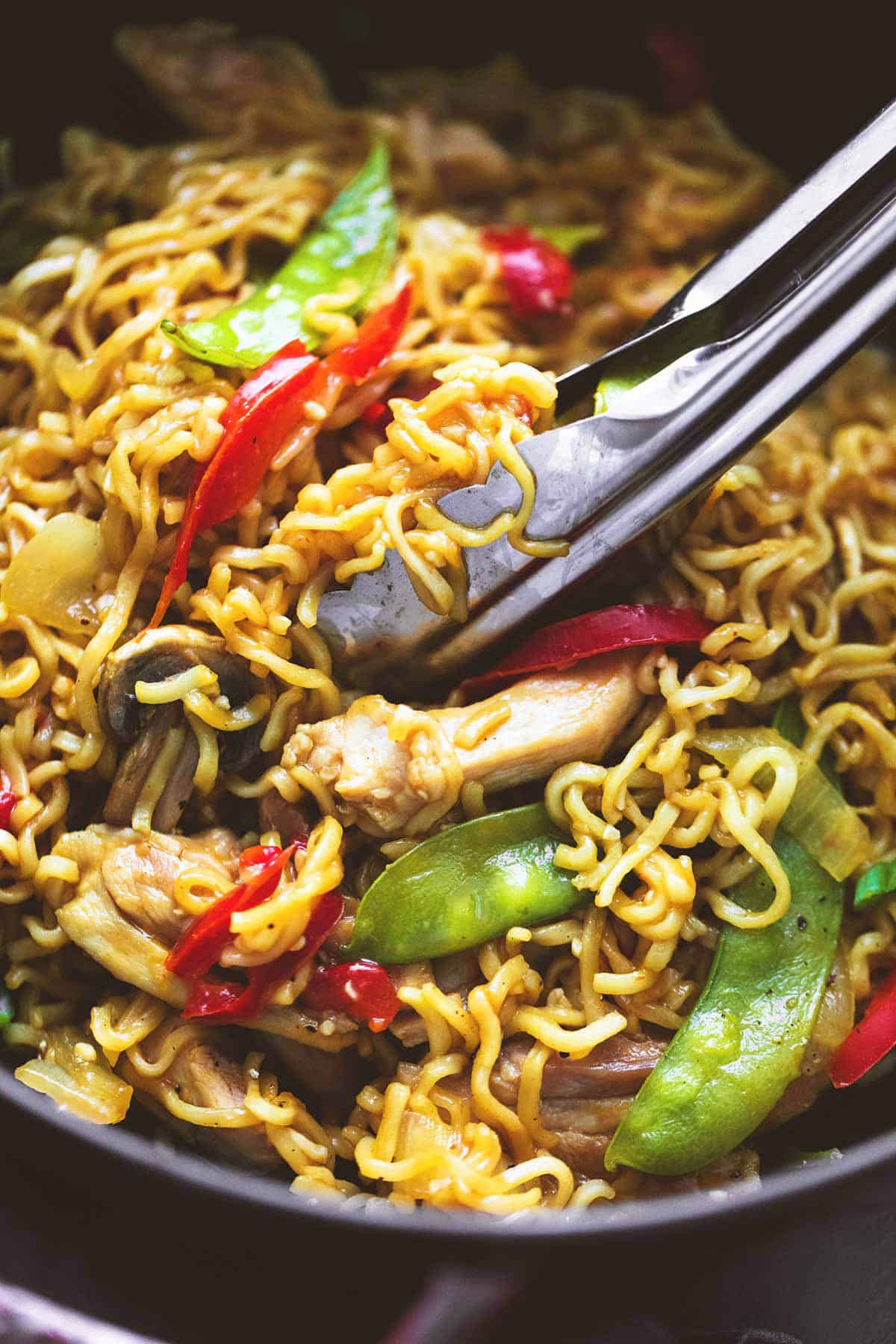 close up of chicken & veggie ramen and tongs.