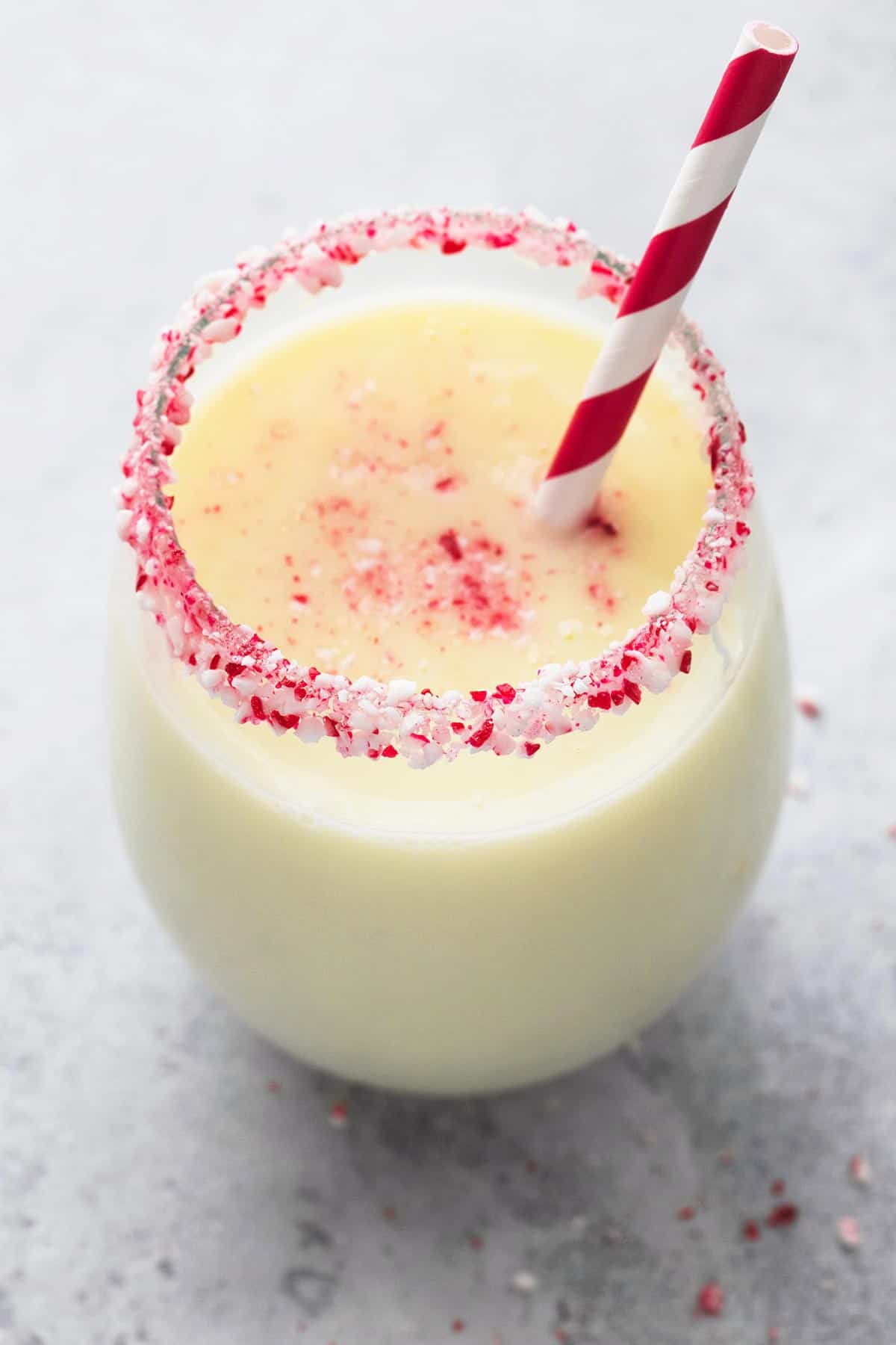 peppermint white hot chocolate in a glass with crushed peppermint candy on the rim with a straw.