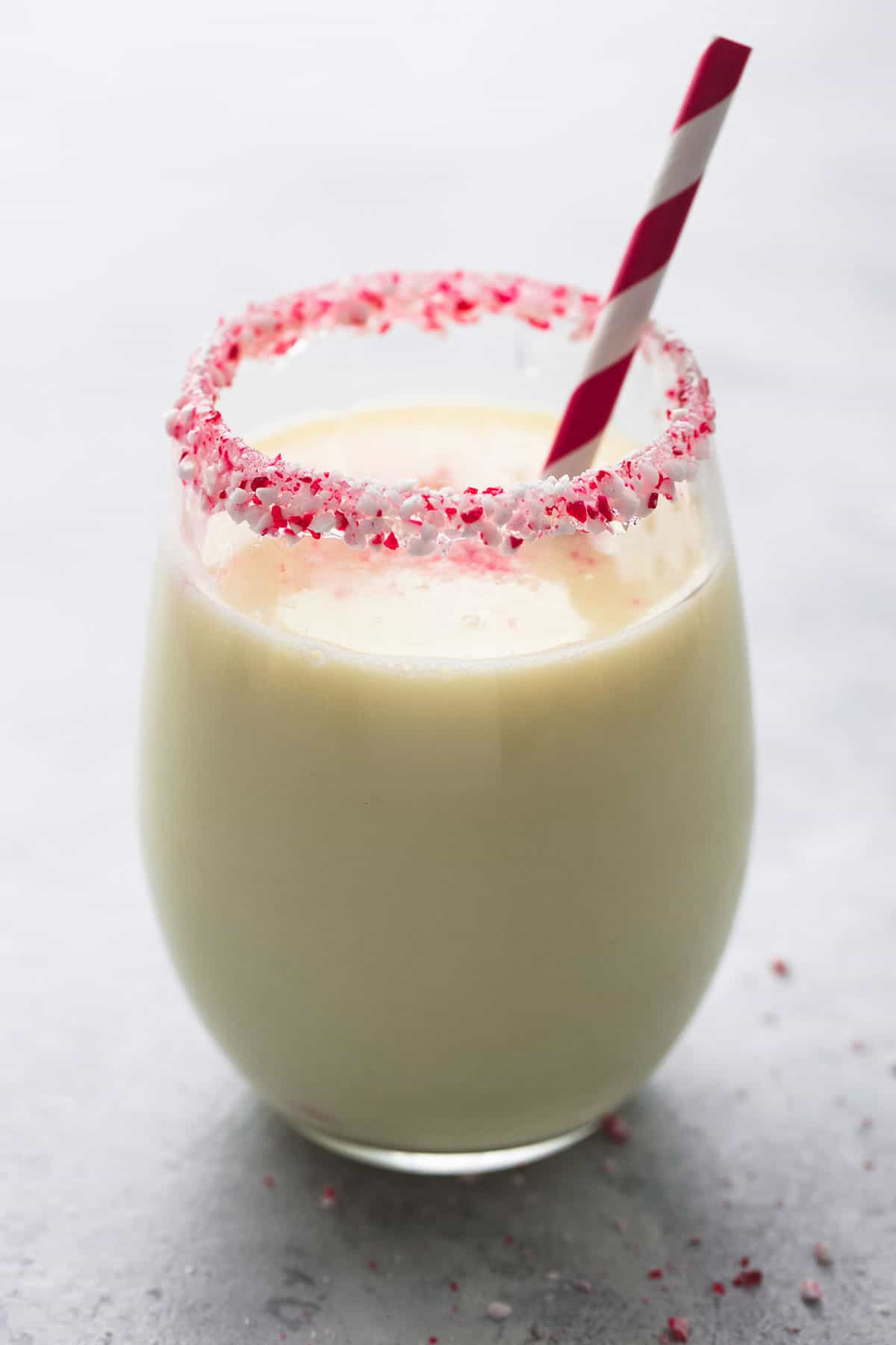 a peppermint white hot chocolate in a glass with crushed up peppermint candy around the rim with a straw.
