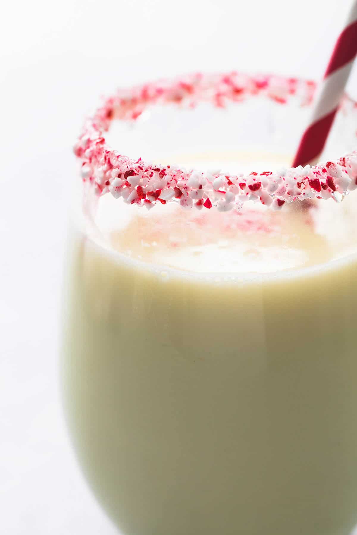 close up of peppermint white hot chocolate in a glass with crushed up peppermint candy around the rim with a straw.