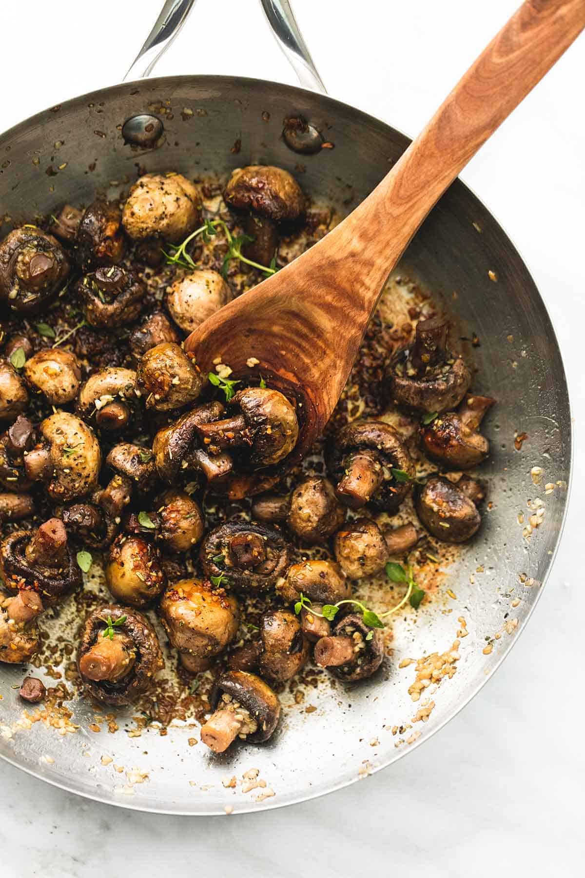 top view of garlic butter mushrooms with a wooden serving spoon in a skillet.