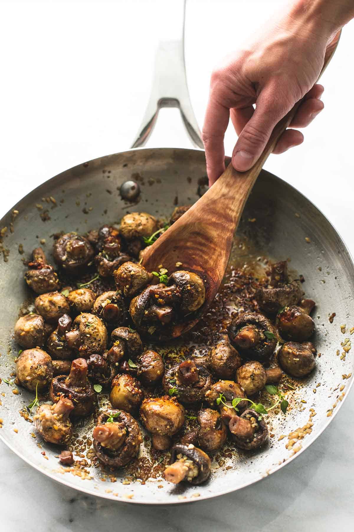 a hand scooping some garlic butter mushrooms with a wooden serving spoon.