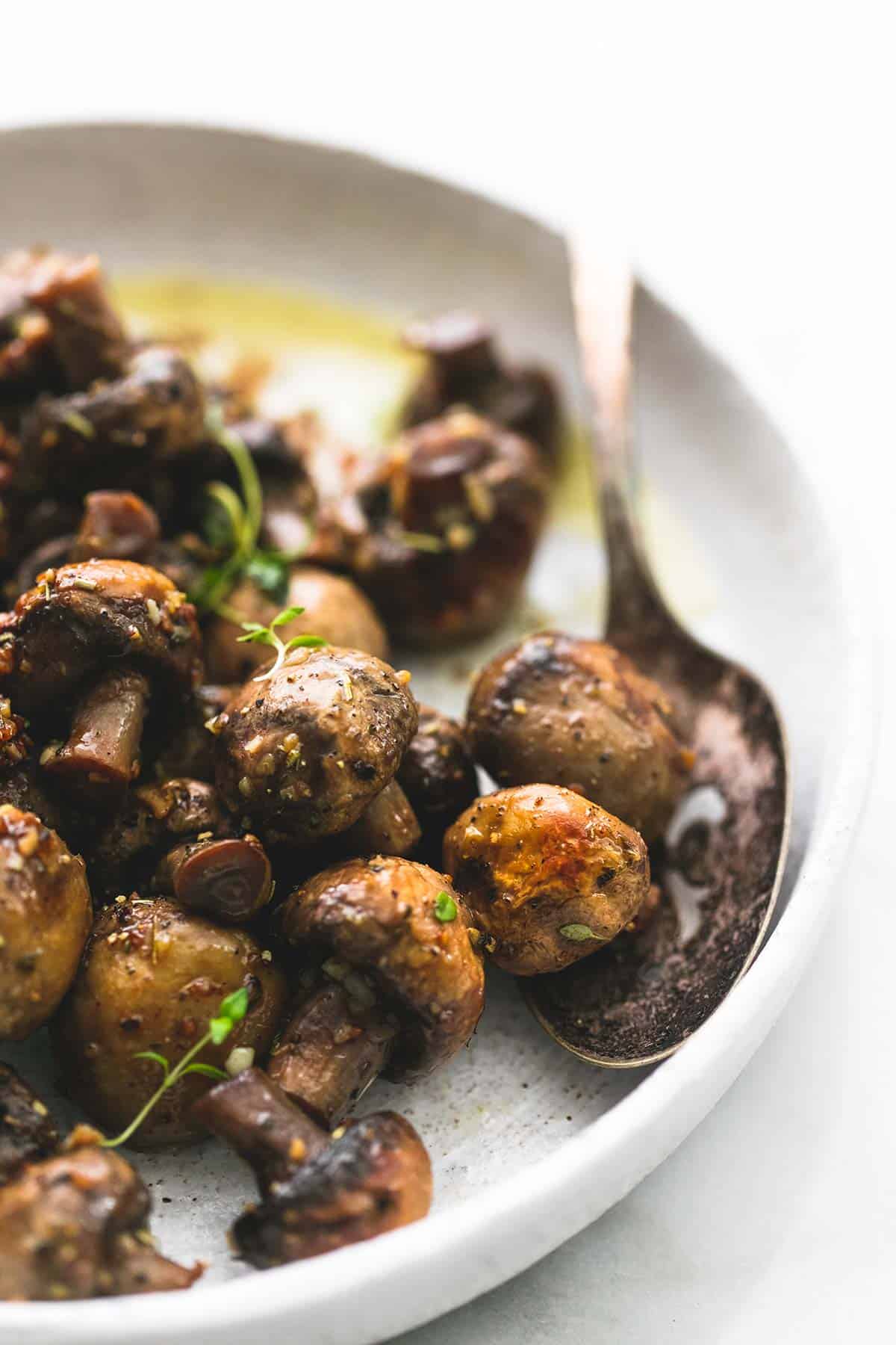 close up of garlic butter mushrooms with a spoon on a plate.