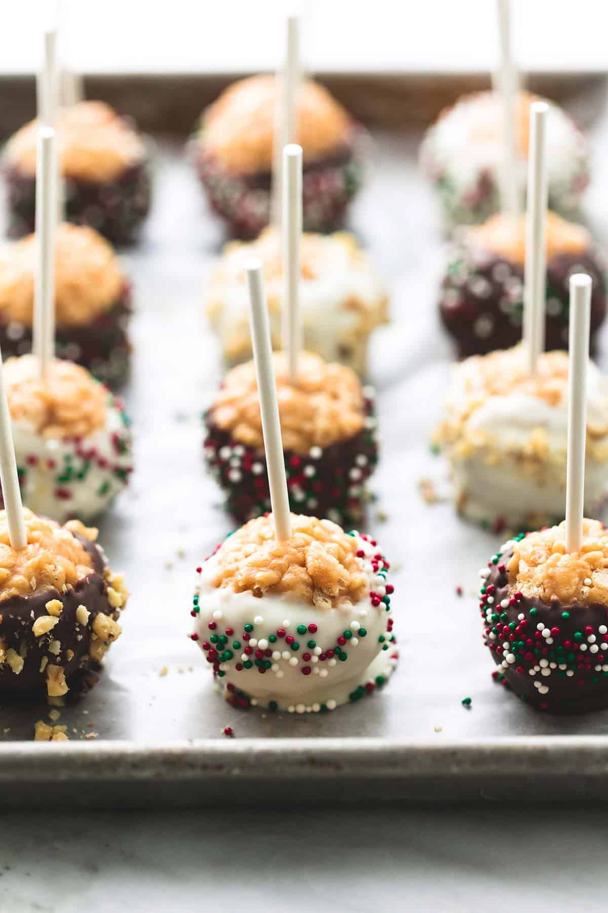scotcheroos on a stick on a baking sheet with some dipped in white chocolate with sprinkles and milk chocolate with sprinkles.
