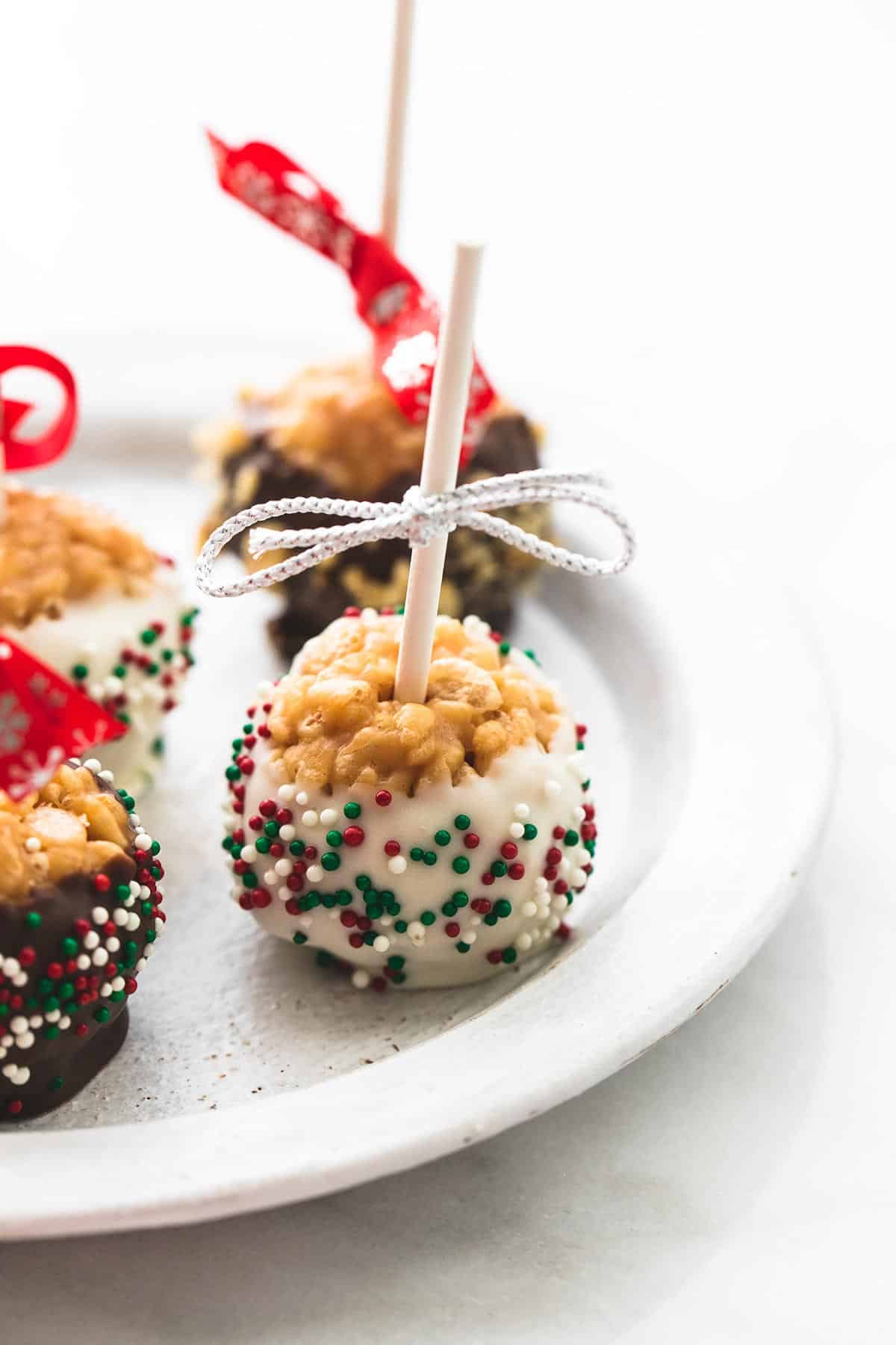 close up of scotcheroos on a stick dipped in white and light chocolate and sprinkles on a plate.