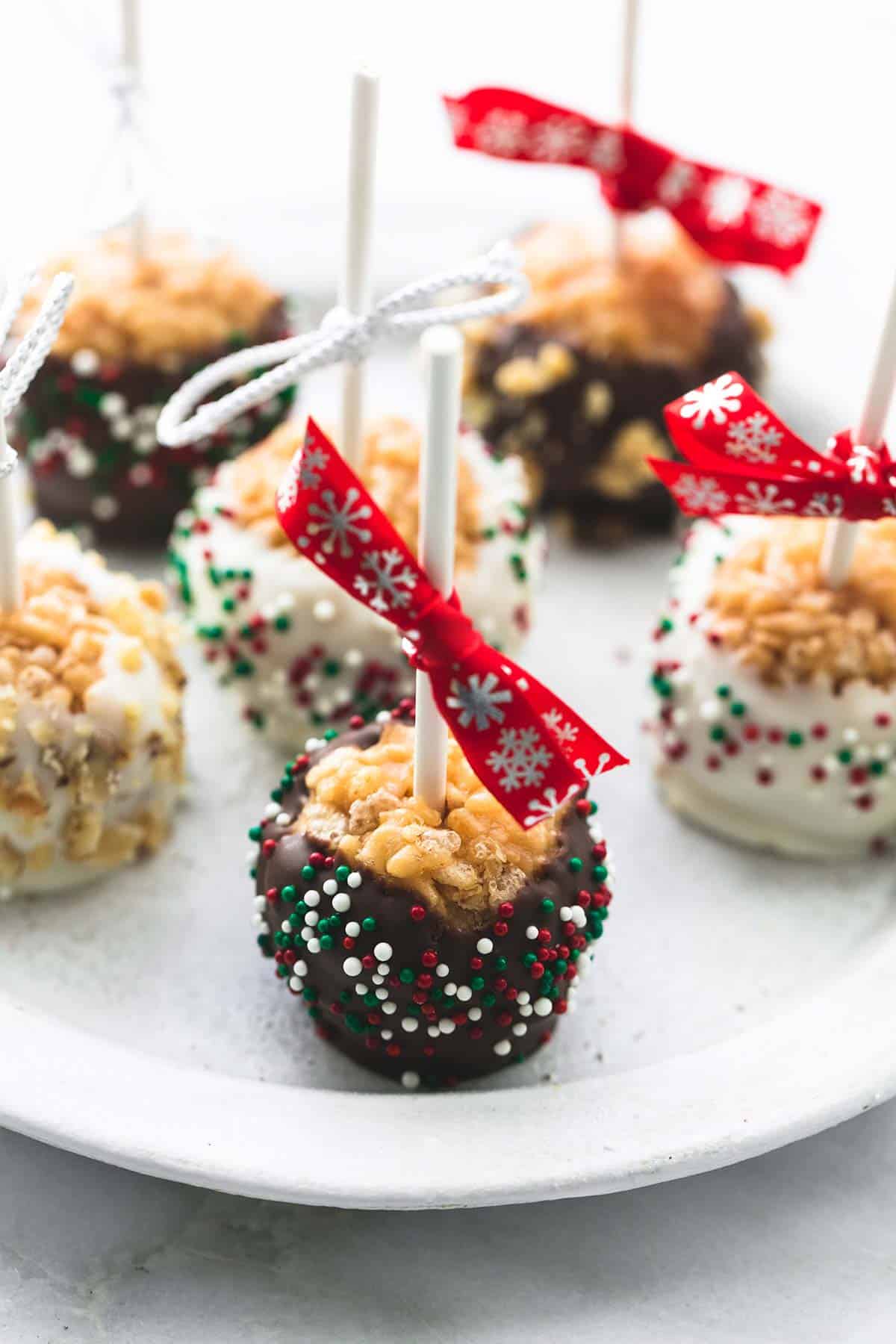 scotcheroos on a stick on a plate with some dipped in white chocolate with sprinkles and milk chocolate with sprinkles.