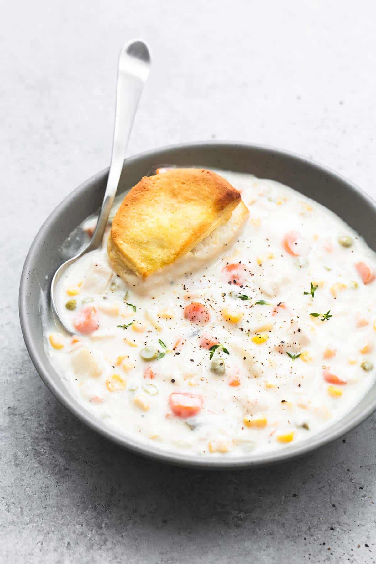 slow cooker chicken pot pie soup with a spoon and a biscuit in a bowl.