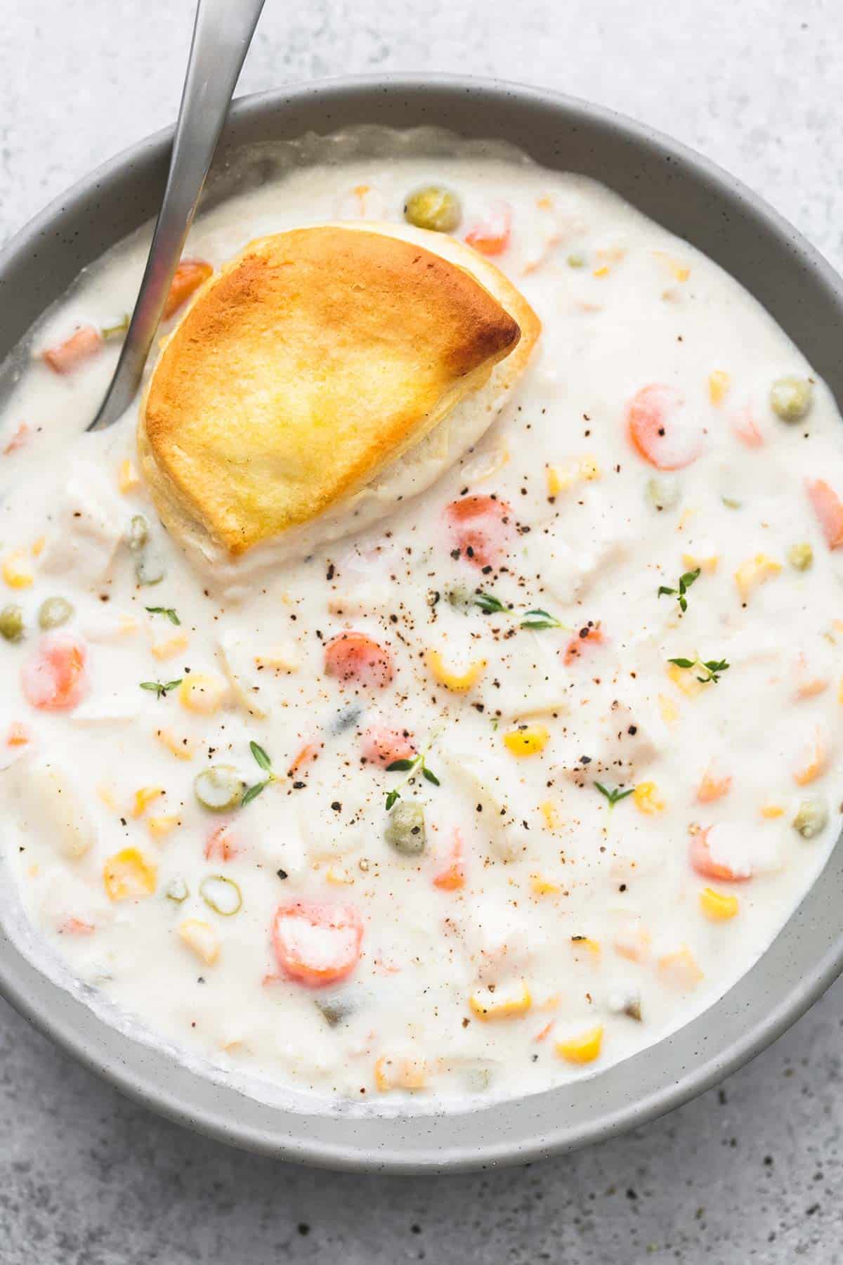 close up top view of slow cooker chicken pot pie soup with a biscuit and a spoon in a bowl.