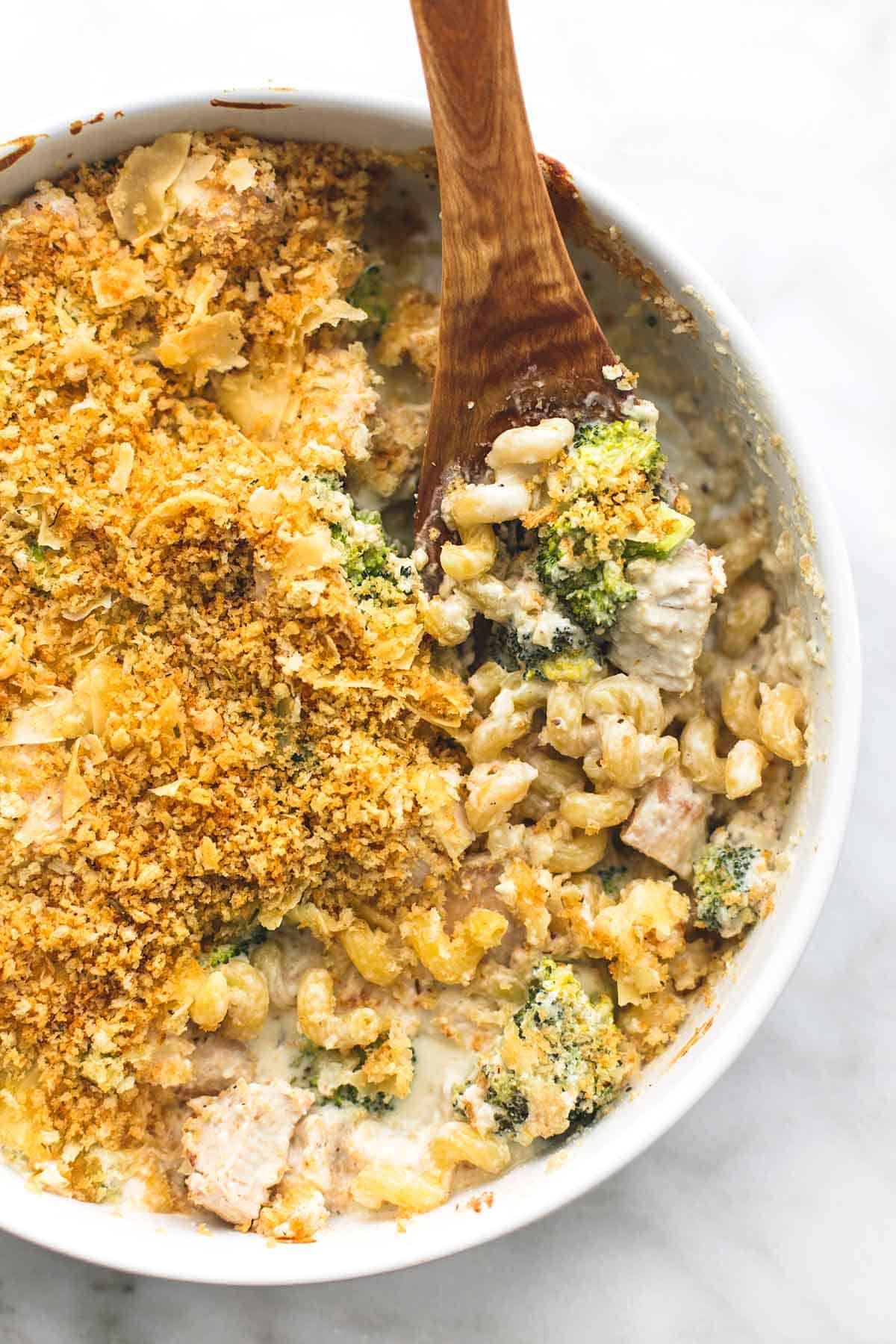 top view of baked chicken broccoli alfredo with a wooden serving spoon in a round serving tray.