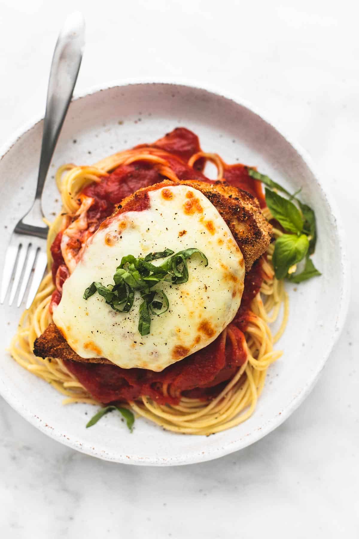 top view of baked chicken parmesan on spaghetti with a fork on a plate.