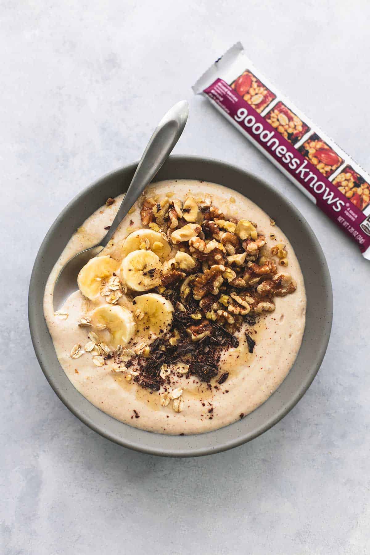 top view of a banana nut smoothie bowl with a spoon in it with a wrapped granola bar on the side.