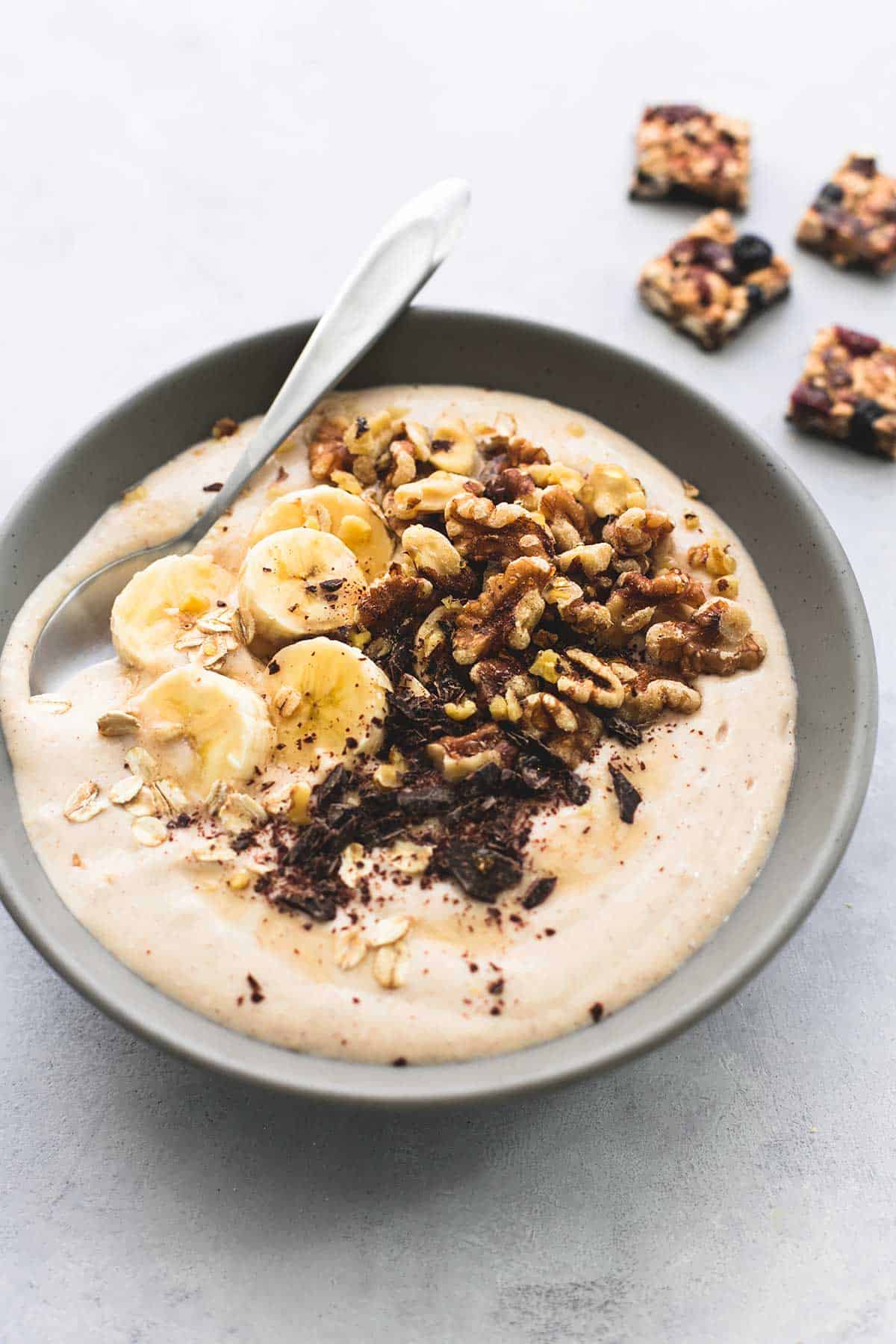 a banana nut smoothie bowl with a spoon in it with granola bar chunks in the background.