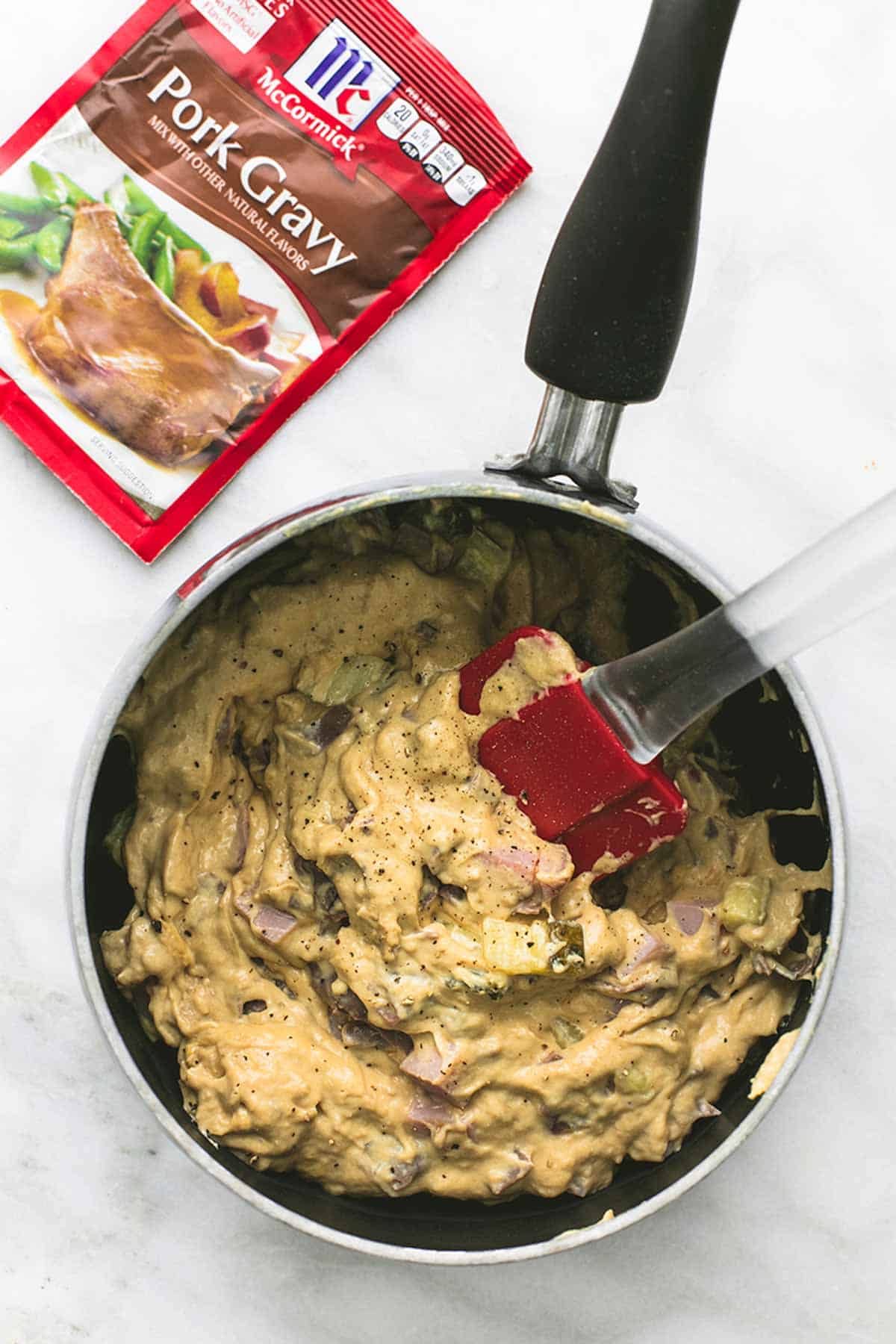 top view of a pan with pork gravy and a rubber spatula with a package of pork gravy on the side.