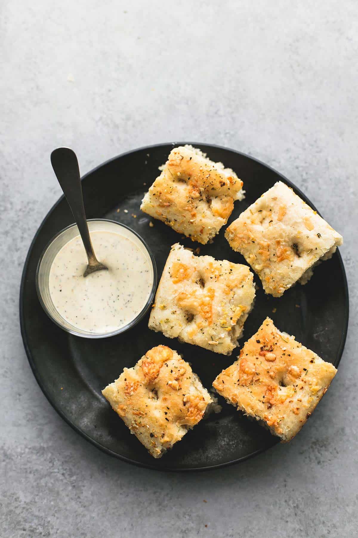 top view of focaccia bread pieces with a bowl of dipping sauce and a spoon on the side all on a plate.