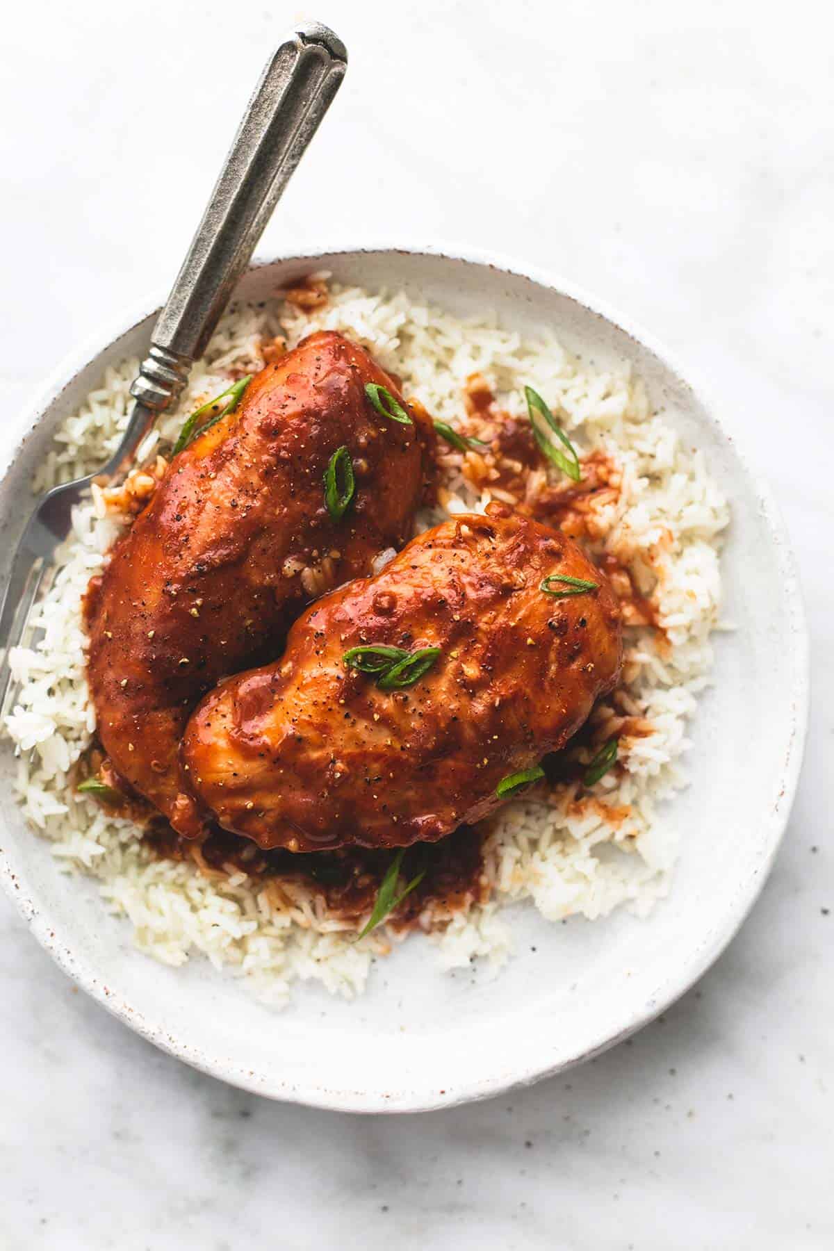 top view of chicken adobo on rice with a fork on a plate.