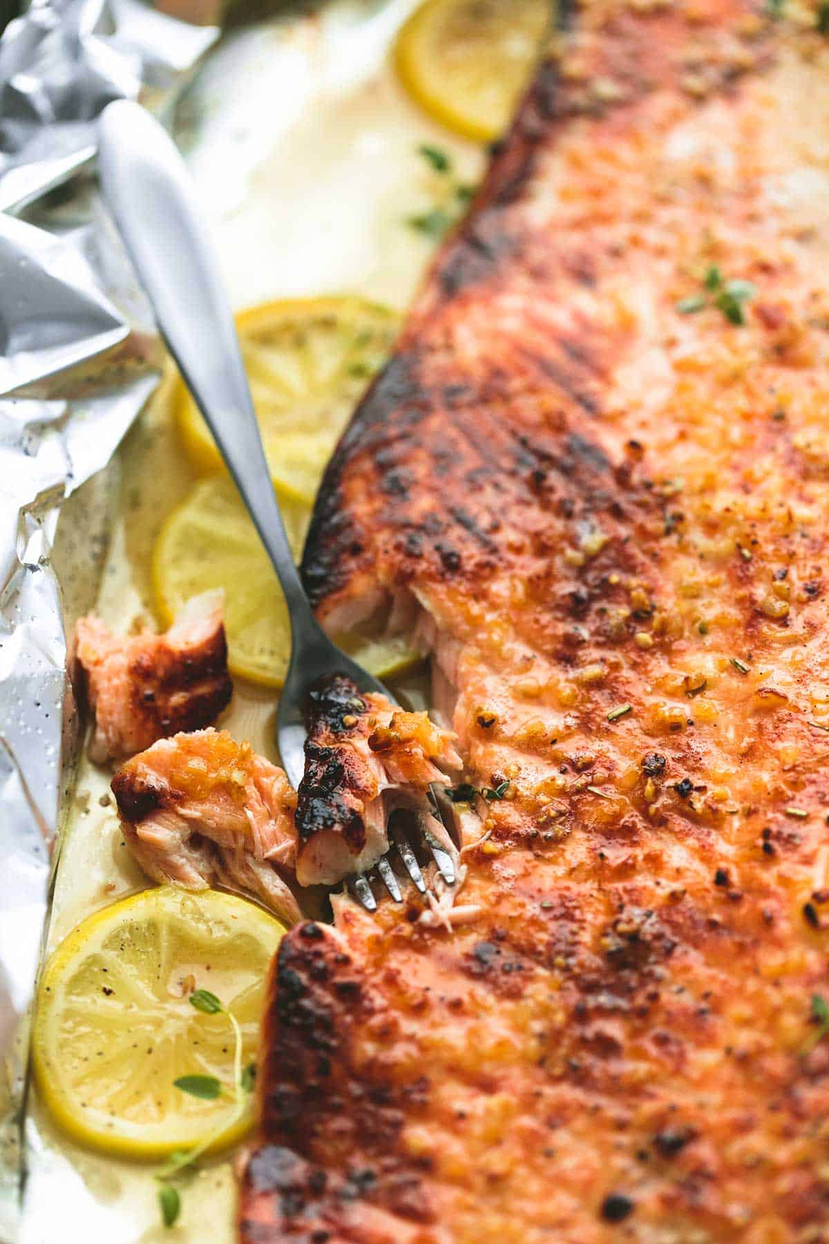 close up of a fork with a bite of salmon sitting next to baked honey lemon garlic salmon in foil with lemon wheels.