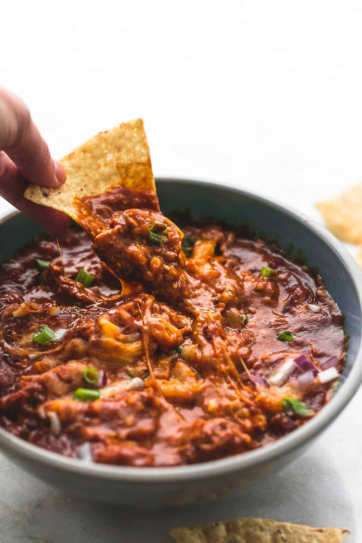 a hand dipping a chip in a bowl of slow cooker bbq chicken dip.